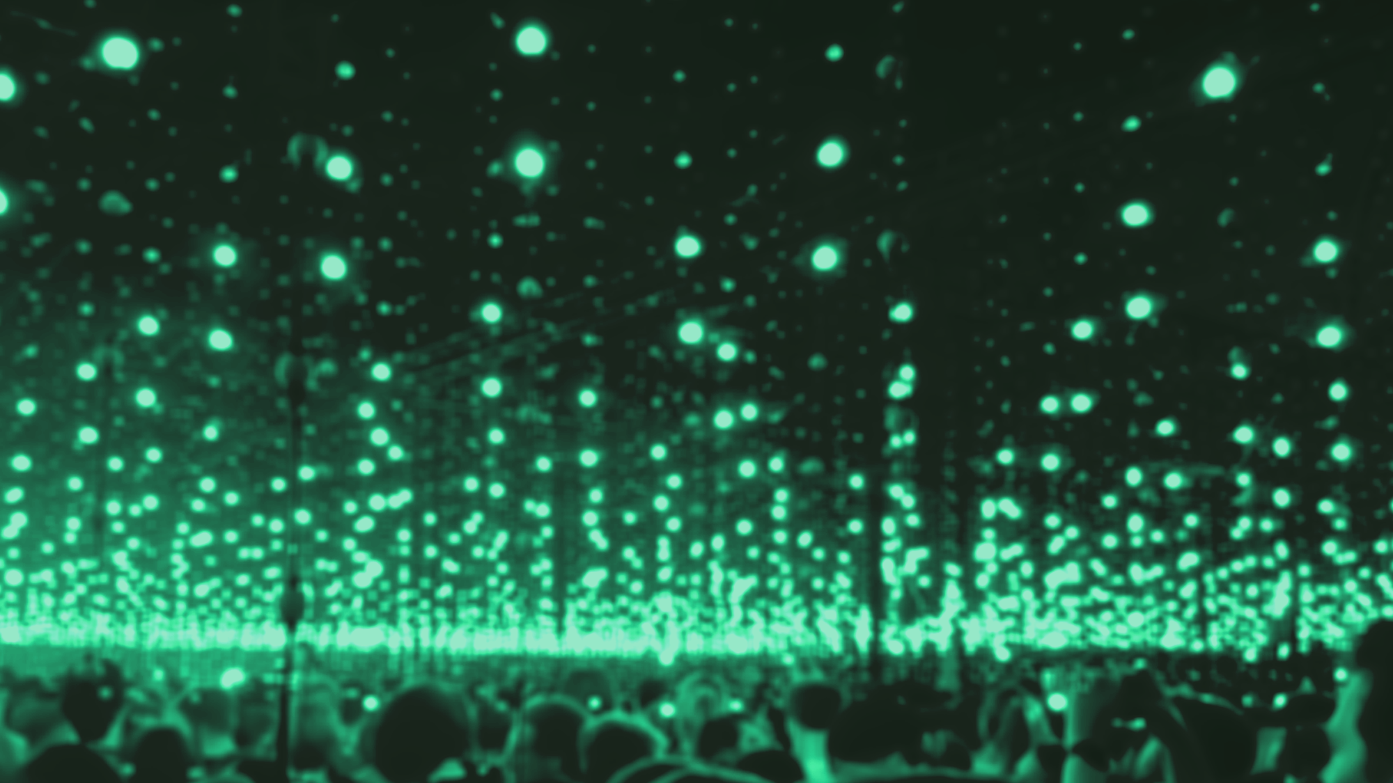 A large indoor crowd attending a concert or event with green stage lighting and hanging green lights creating a futuristic ambiance.