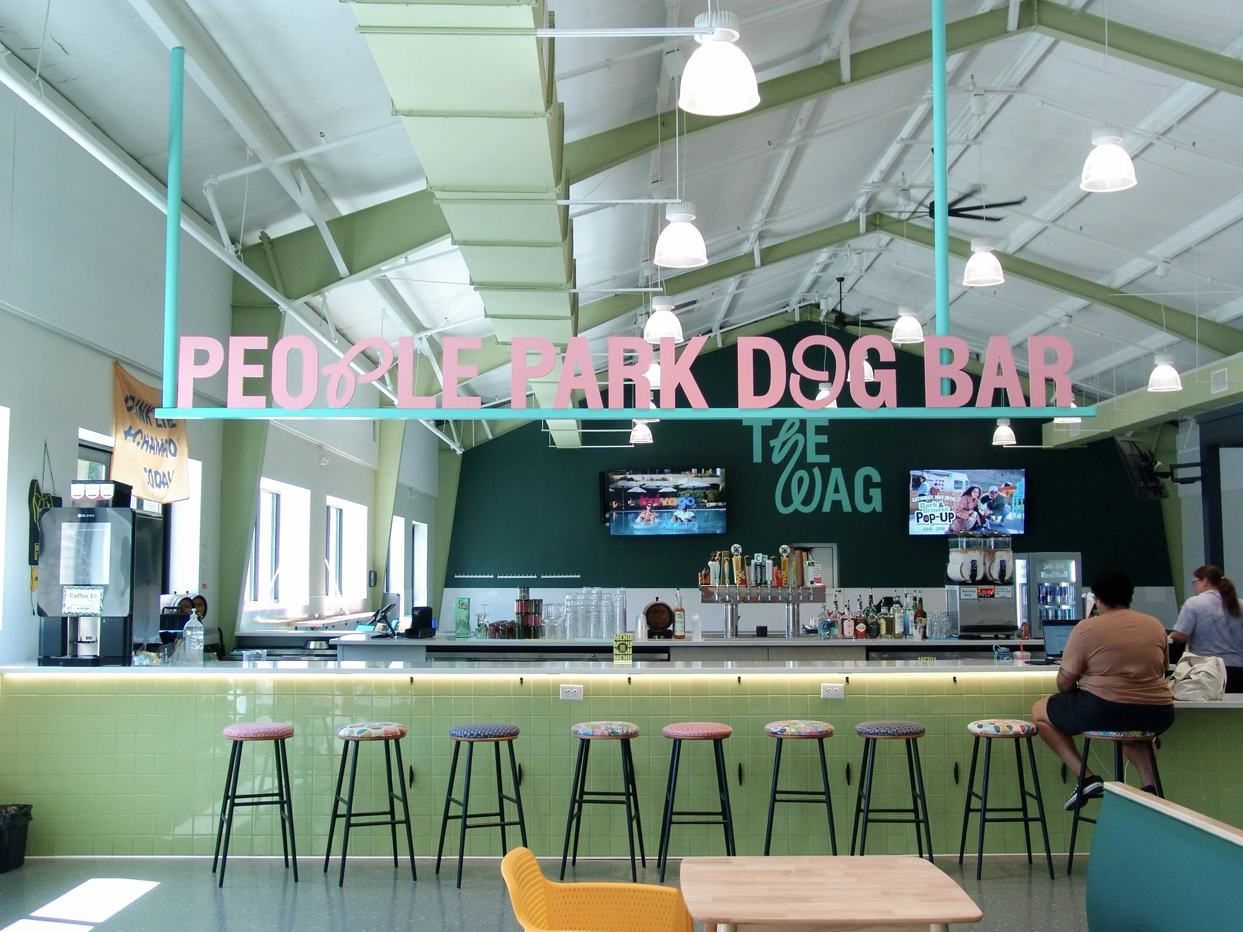 Pink and teal sign reading "People Park Dog Bar" hanging above a green bar counter. Sign created by Brite Line Signs in Columbus, Ohio