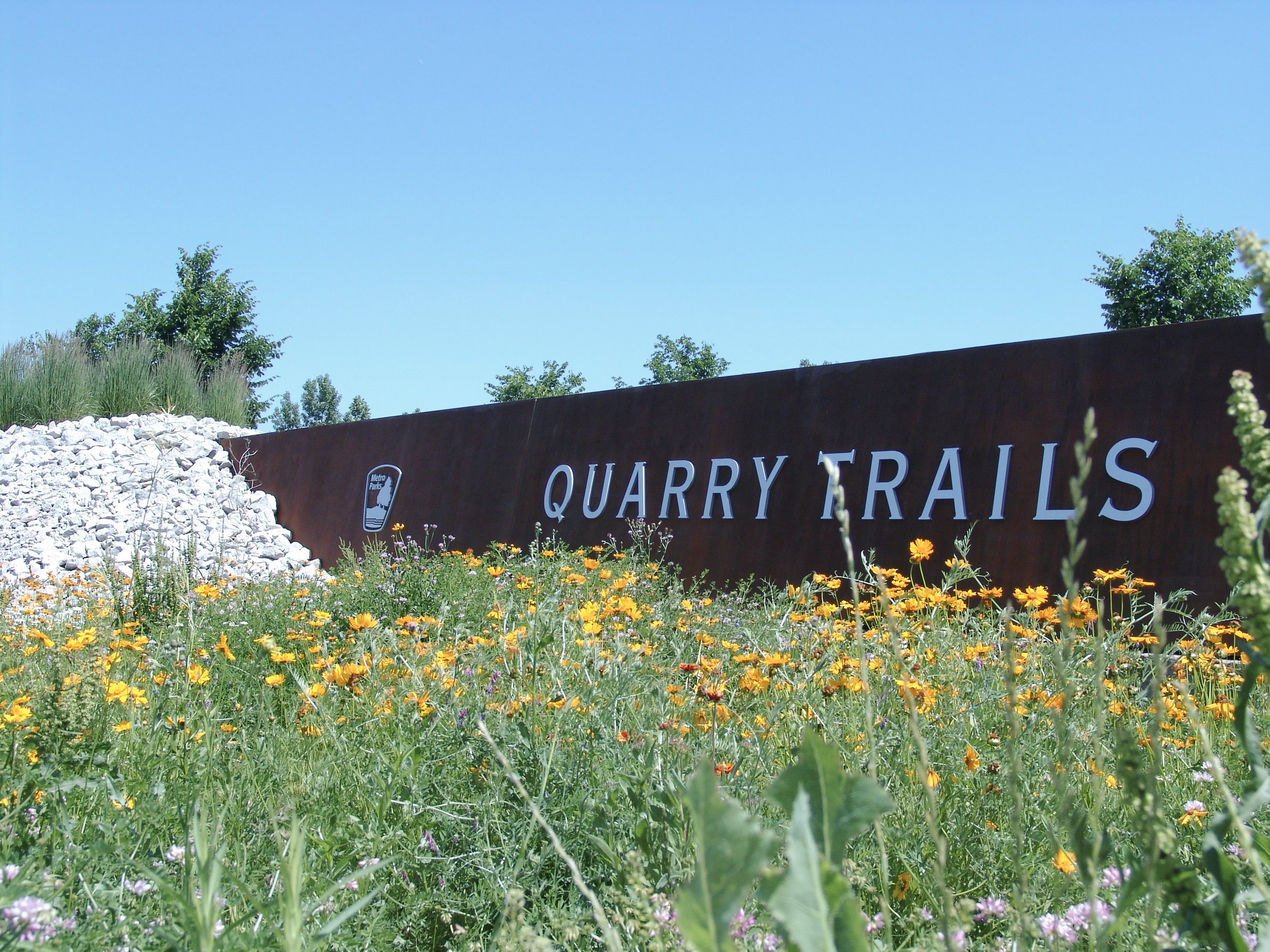 Rustic sign reading "Quarry Trails" emerging from pile of rocks. Sign created by Brite Line Signs in Columbus, Ohio