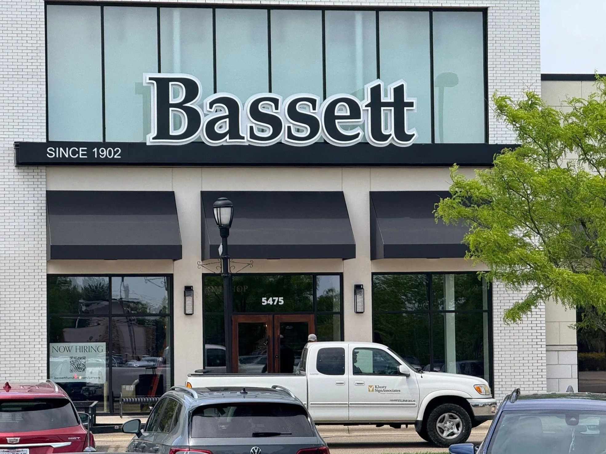 Black and white sign reading "Bassett" hangs on the side of a building with trucks underneath. Sign created by Brite Line Signs in Columbus, Ohio