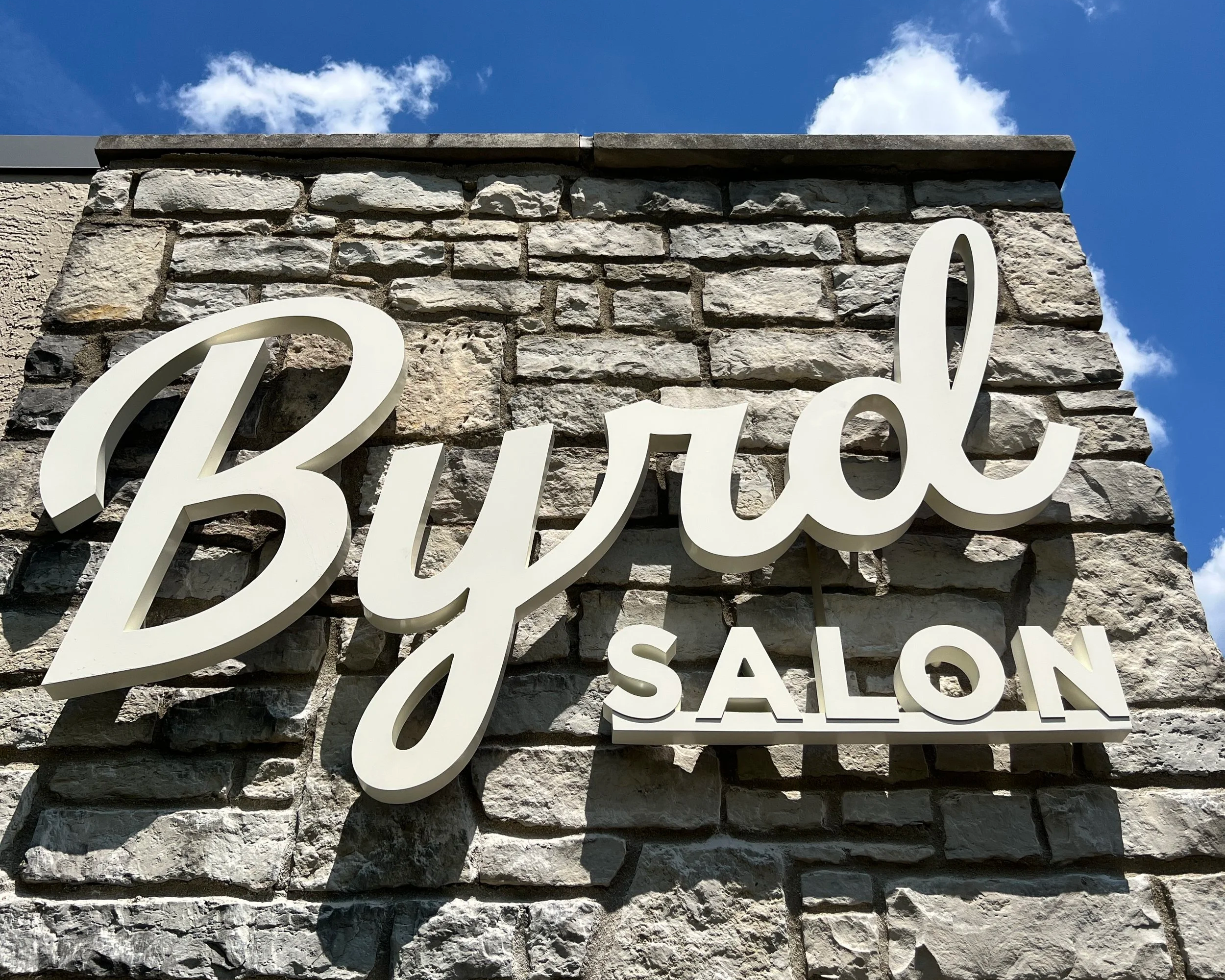 White sign reading "Byrd Salon" on textured wall. Created by Brite Line Signs in Columbus, Ohio.
