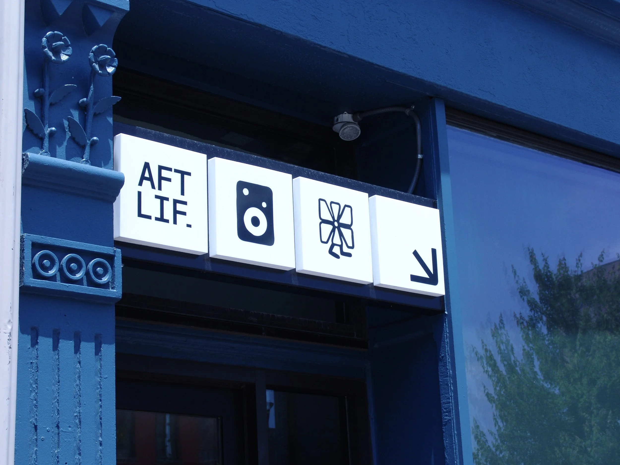 Miniature illuminated squares reading "AFTLIFE" and showing various icons mounted to a blue building. Sign created by Brite Line Signs in Columbus, Ohio