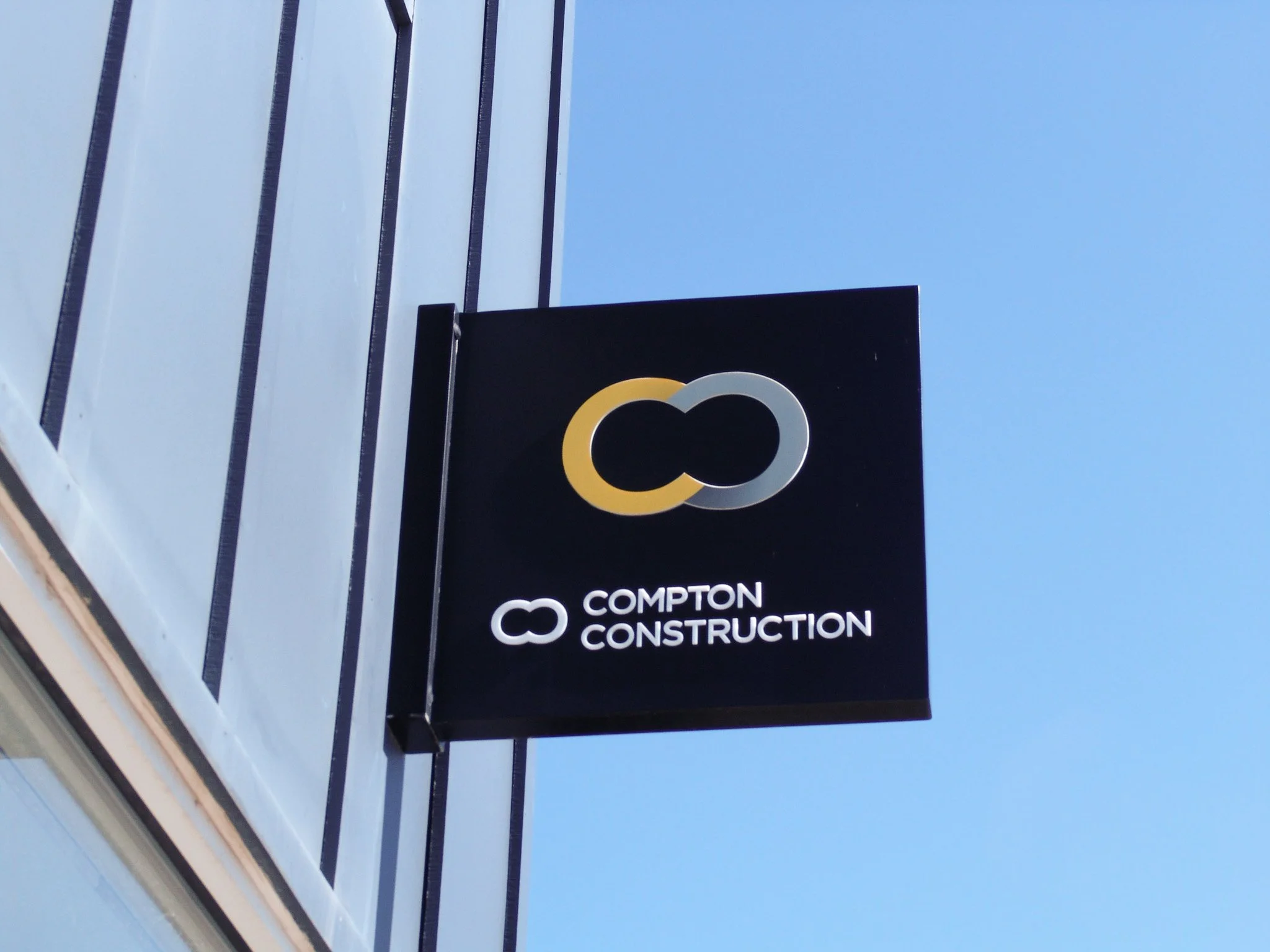 Rectangular blade sign reading "Compton Construction" hanging on side of building, created by Brite Line Signs in Columbus, Ohio