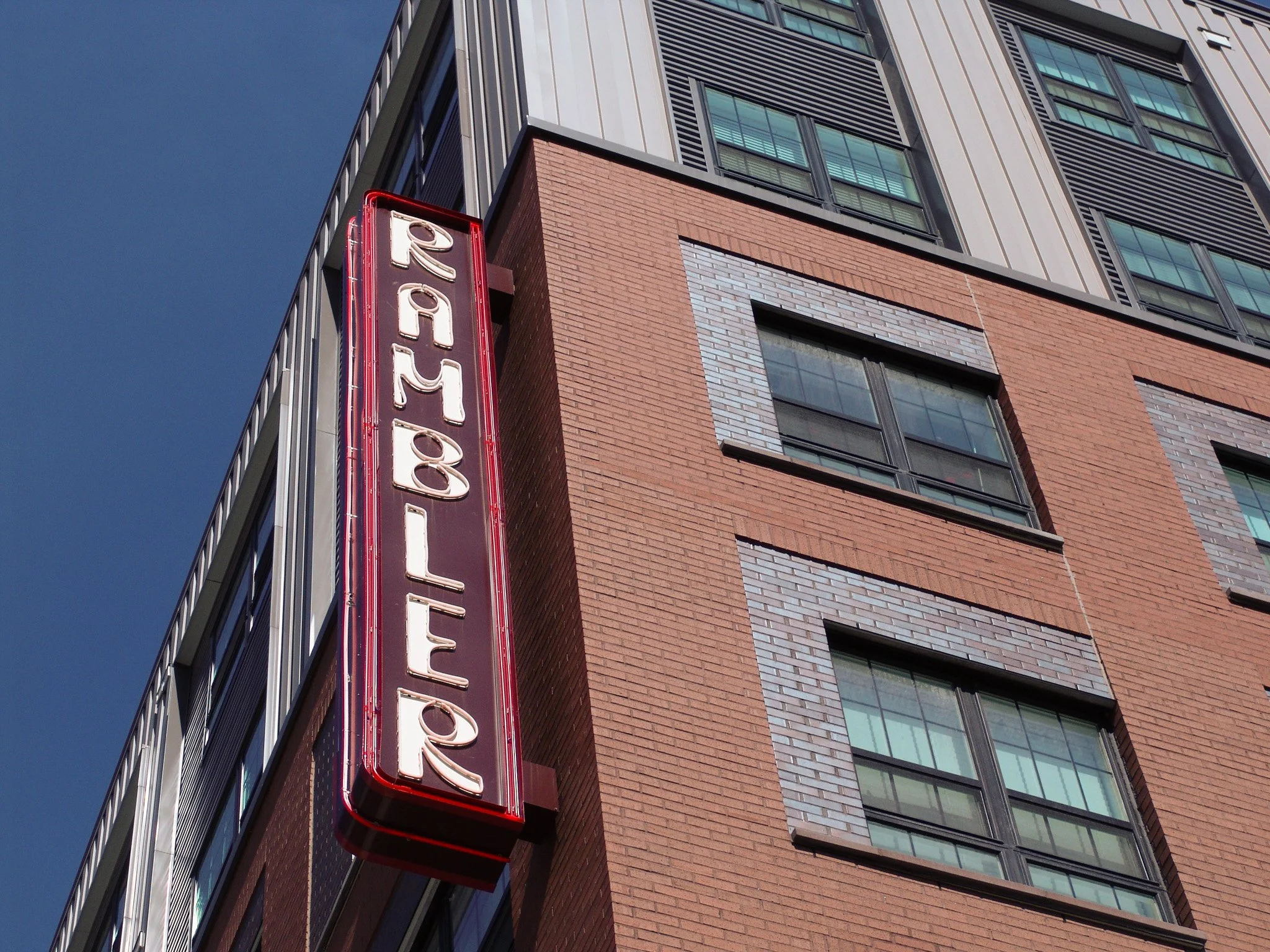 Vertical red and black neon sign reading "Rambler" hanging on brick building. Sign created by Brite Line Signs in Columbus, Ohio