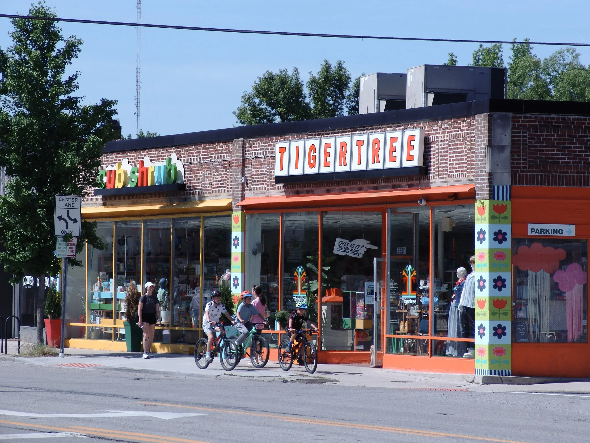 Signs on a brick building reading "Tigertree" and "Cubshrub," group of people biking past. Sign created by Brite Line Signs in Columbus, Ohio