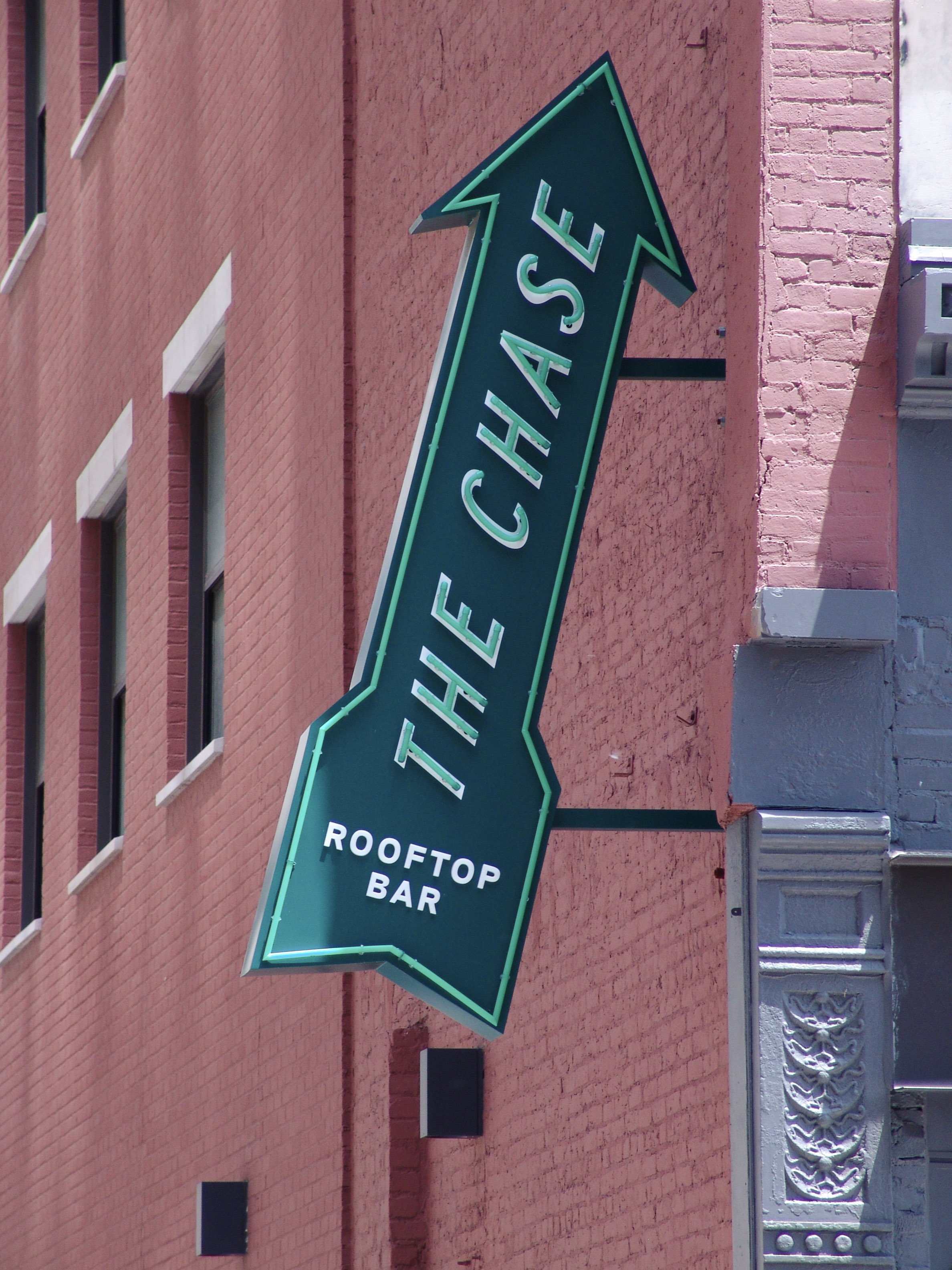 Green neon sign reading "The Chase" mounted to side of red brick building, created by Brite Line Signs in Columbus, Ohio