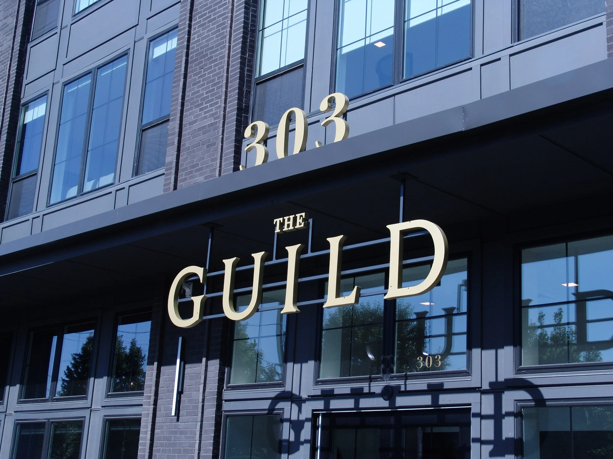 Gold letters reading "The Guild" placed on a blue and black building, "303" above. Sign created by Brite Line Signs in Columbus, Ohio