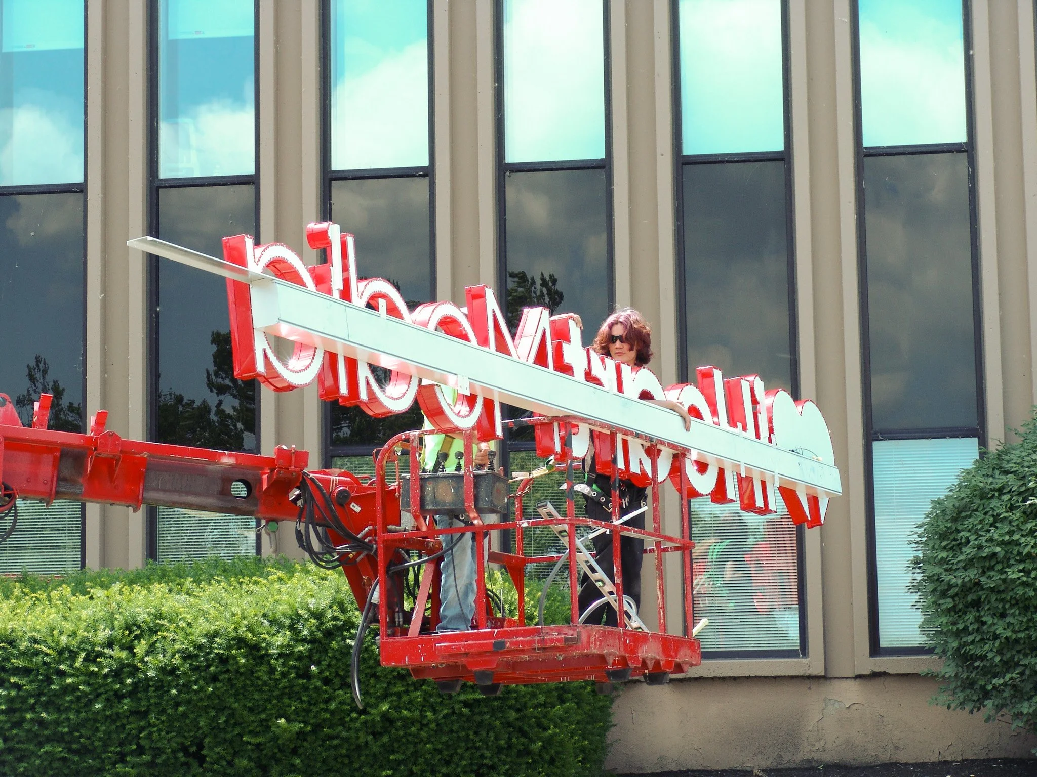 Two people on crane holding sign reading "iheartmedia" backwards. Created by Brite Line Signs in Columbus, OH