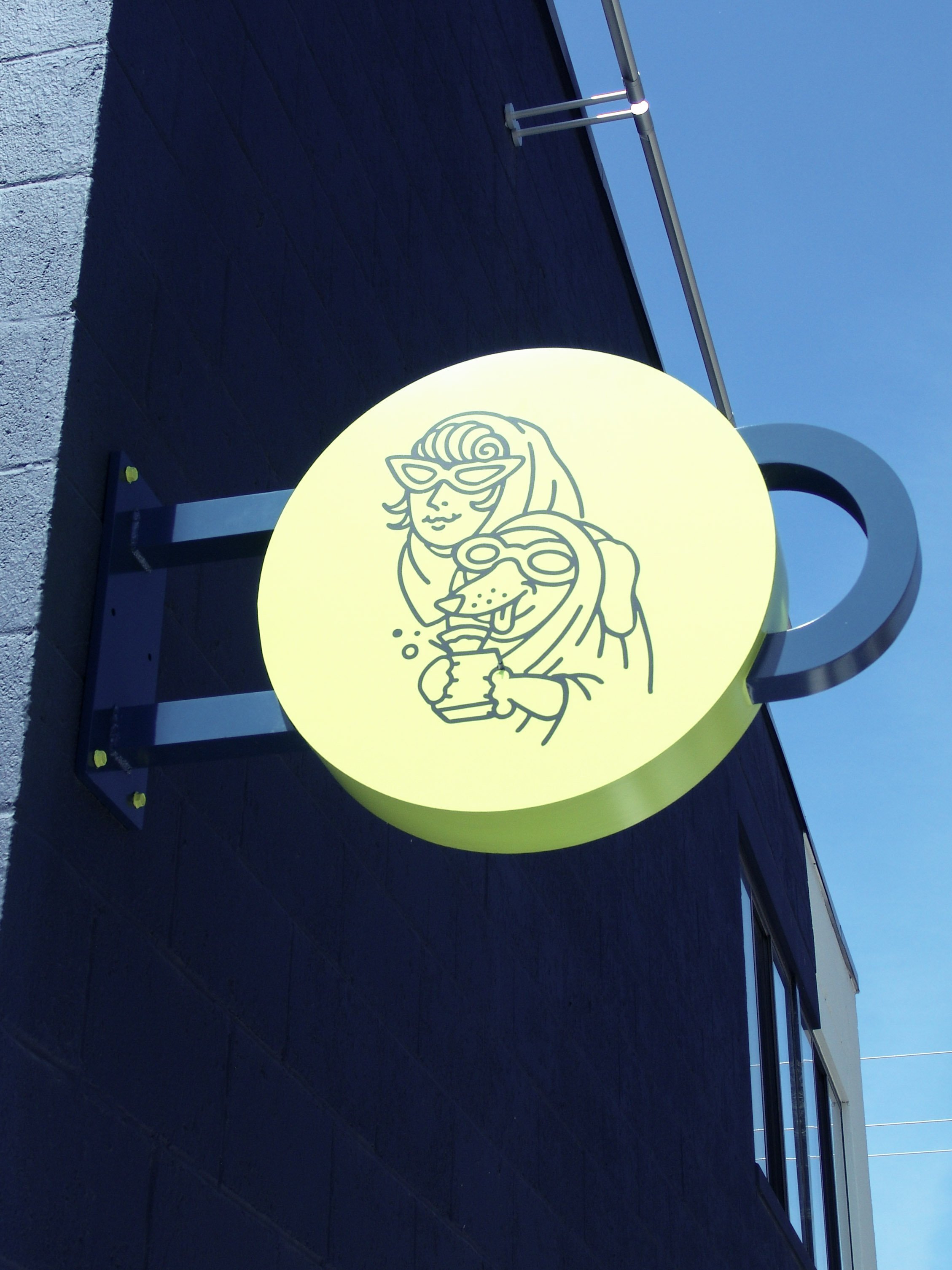 Green circular blade sign with illustration of woman and dog sits on side of a building, created by Brite Line Signs in Columbus, Ohio