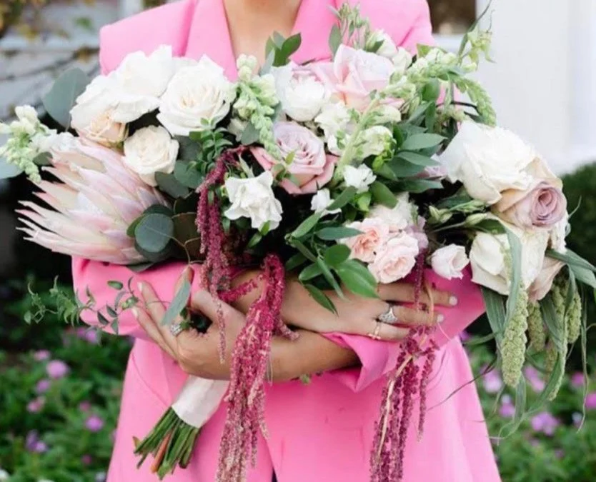 A lady wearing a pink suit holding multiple bouquets