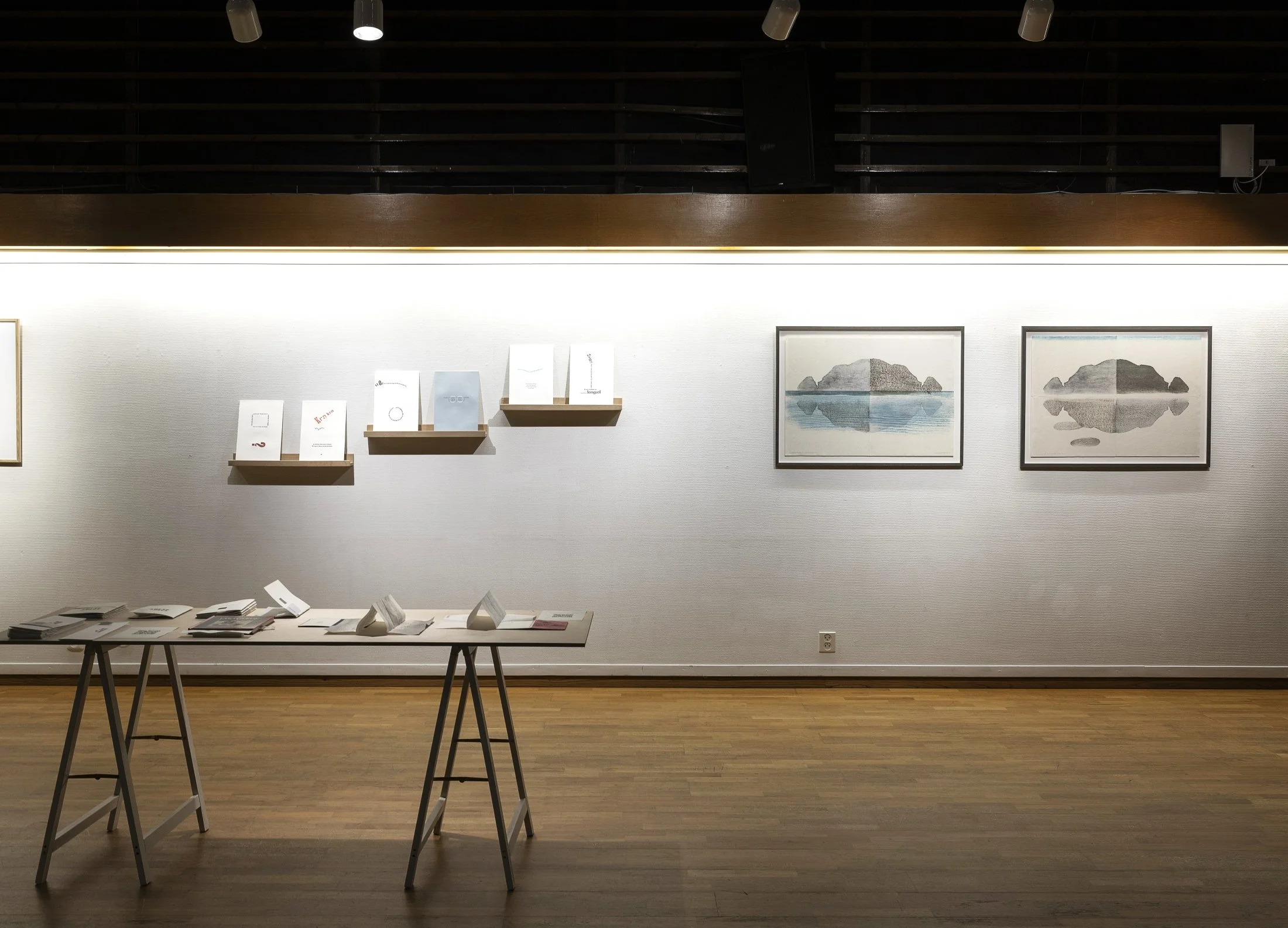 Frå «Ord i veg(g)en» 2025 (gruppeutstilling Anne-Lise Stenseth, Aud Marit Skarrebo Holmen, Karen Helga Maurstig). På bilde nokre av mine arbeid – bord med fanzinar og artists’ books. På veggen «Fuglemøte i kvardagen» boktrykk. To tresnitt. Foto Thor 