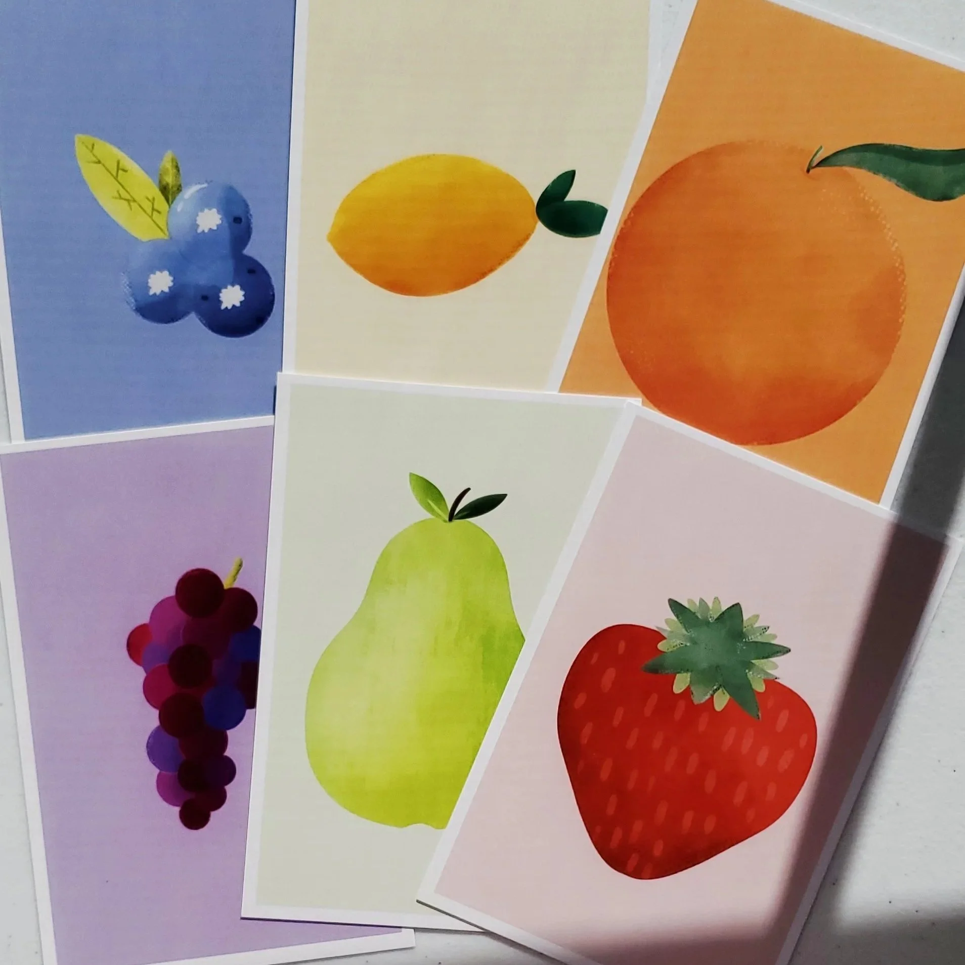 Colorful cards with illustrations of different fruits, including blueberries, lemon, orange, grapes, pear, and strawberry.