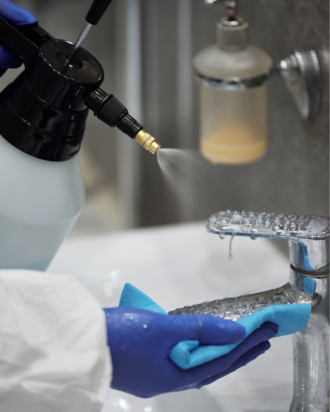 A person wearing blue gloves disinfecting a kitchen faucet with a spray bottle.