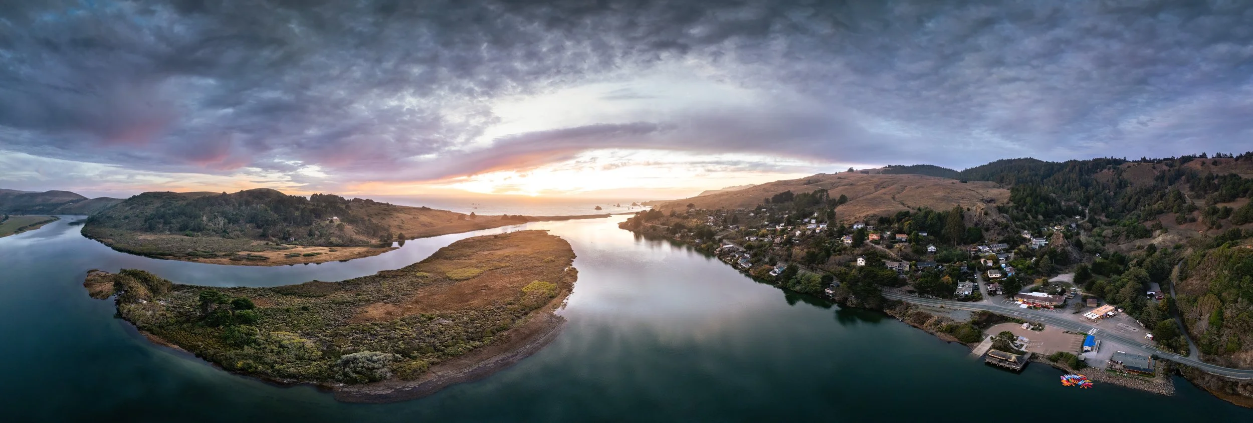 Panoramic view of a river winding through hills at sunset with a small town on the hillside.