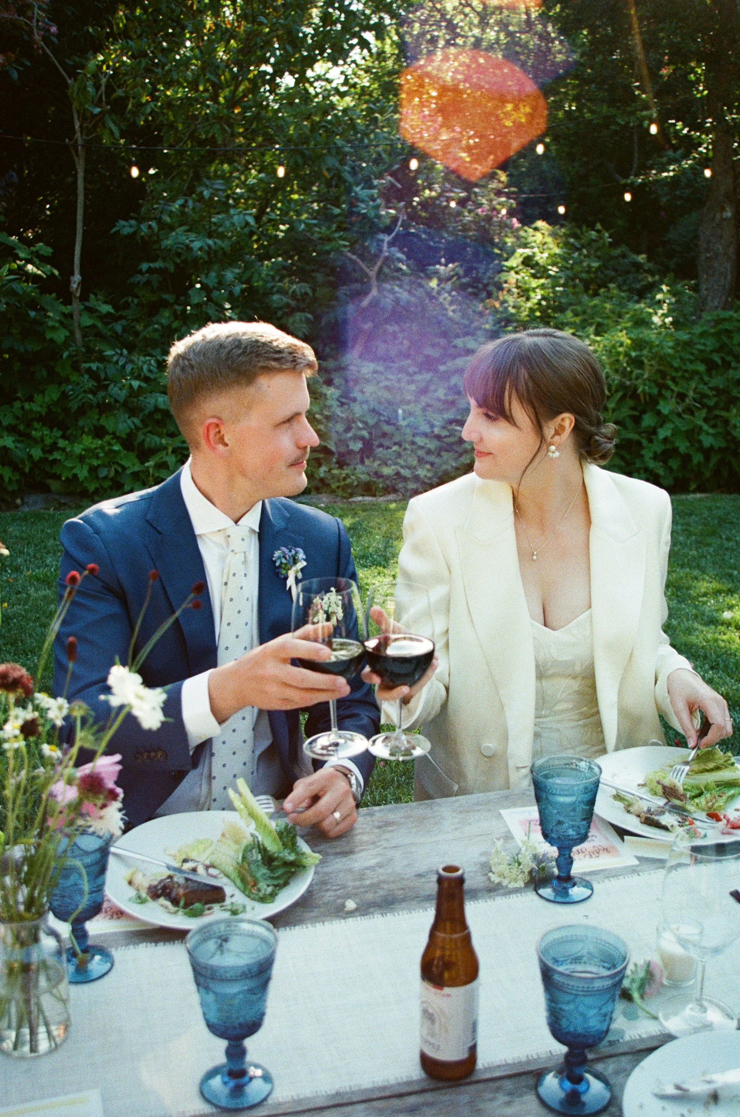 A scenic landscape featuring a large body of turquoise water in the foreground, surrounded by grassy hills and green vegetation, with tall mountain ranges and a cloudy sky in the background.
