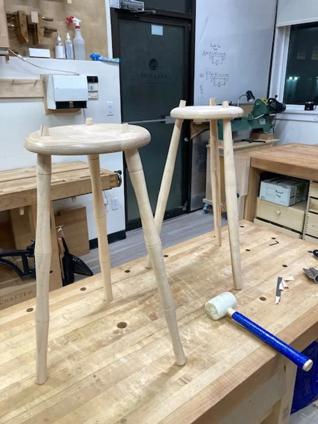 Two round stools being assembled on top of a solid wood workbench