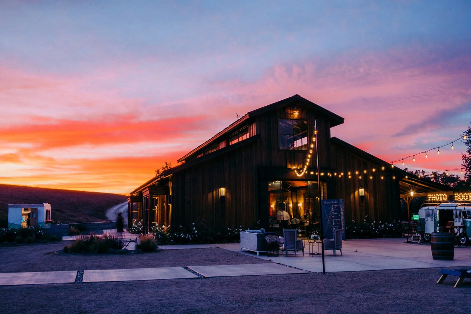 Flying Caballos Ranch Barn exterior at sunset with string lights and orange-pink sky, San Luis Obispo wedding venue photography
