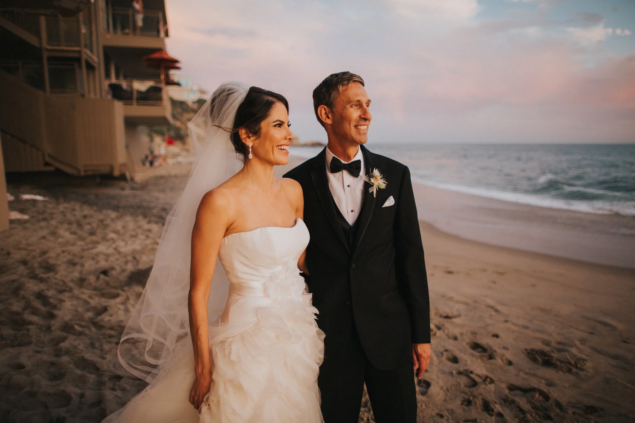 Bride and groom smiling together on the beach at sunset.