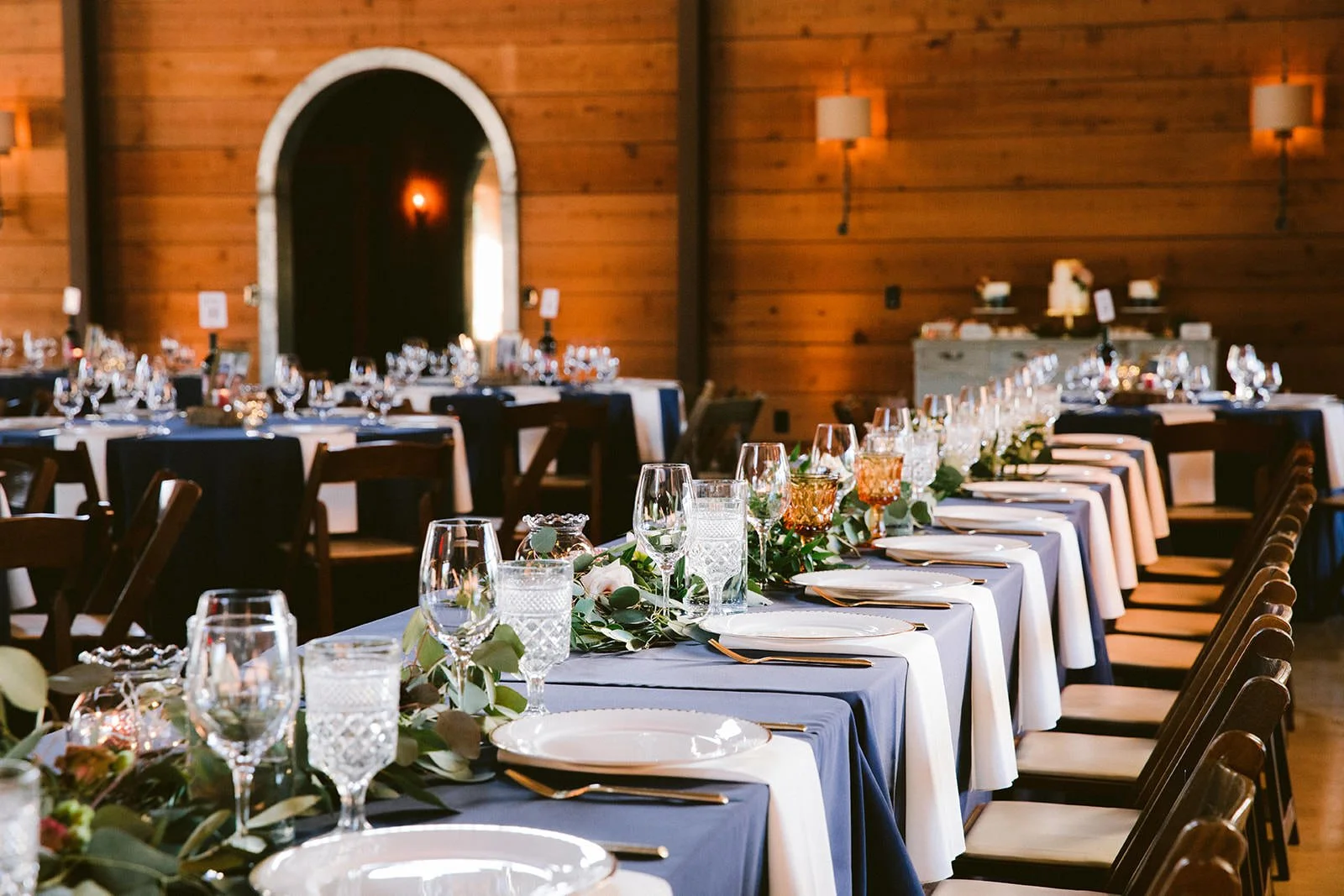 Flying Caballos Ranch Barn interior reception setup with navy blue linen tables, greenery runners, and candlelight, San Luis Obispo wedding photography