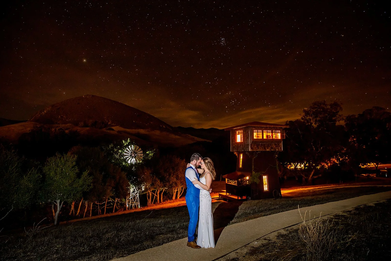 Bride and groom under a starry sky at Flying Caballos Ranch with the glowing Water Tower and Islay Hill at night, San Luis Obispo wedding photographer Michael Stephens