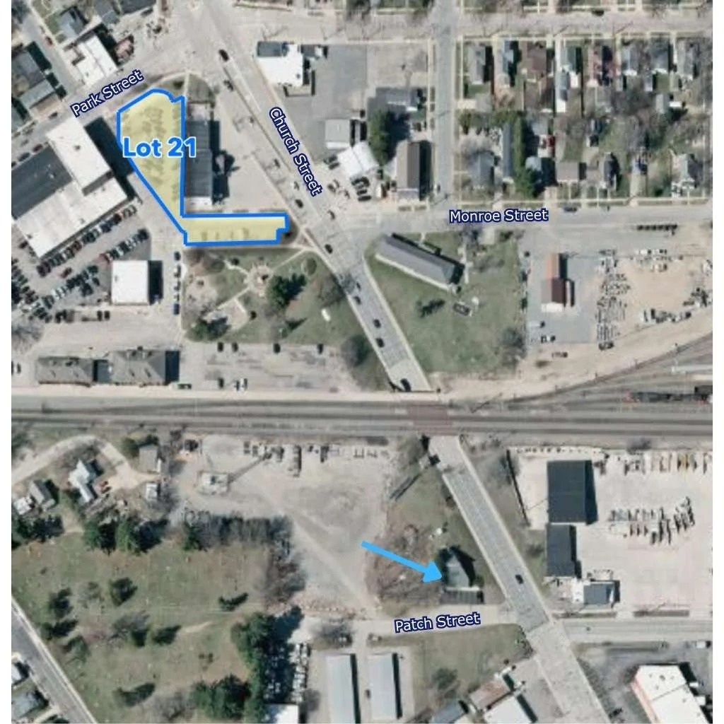 Aerial view of a neighborhood showing streets and buildings, with Lot 21 outlined in blue on the corner of Church Street and Park Street, and a small building on Patch Street marked with an arrow.