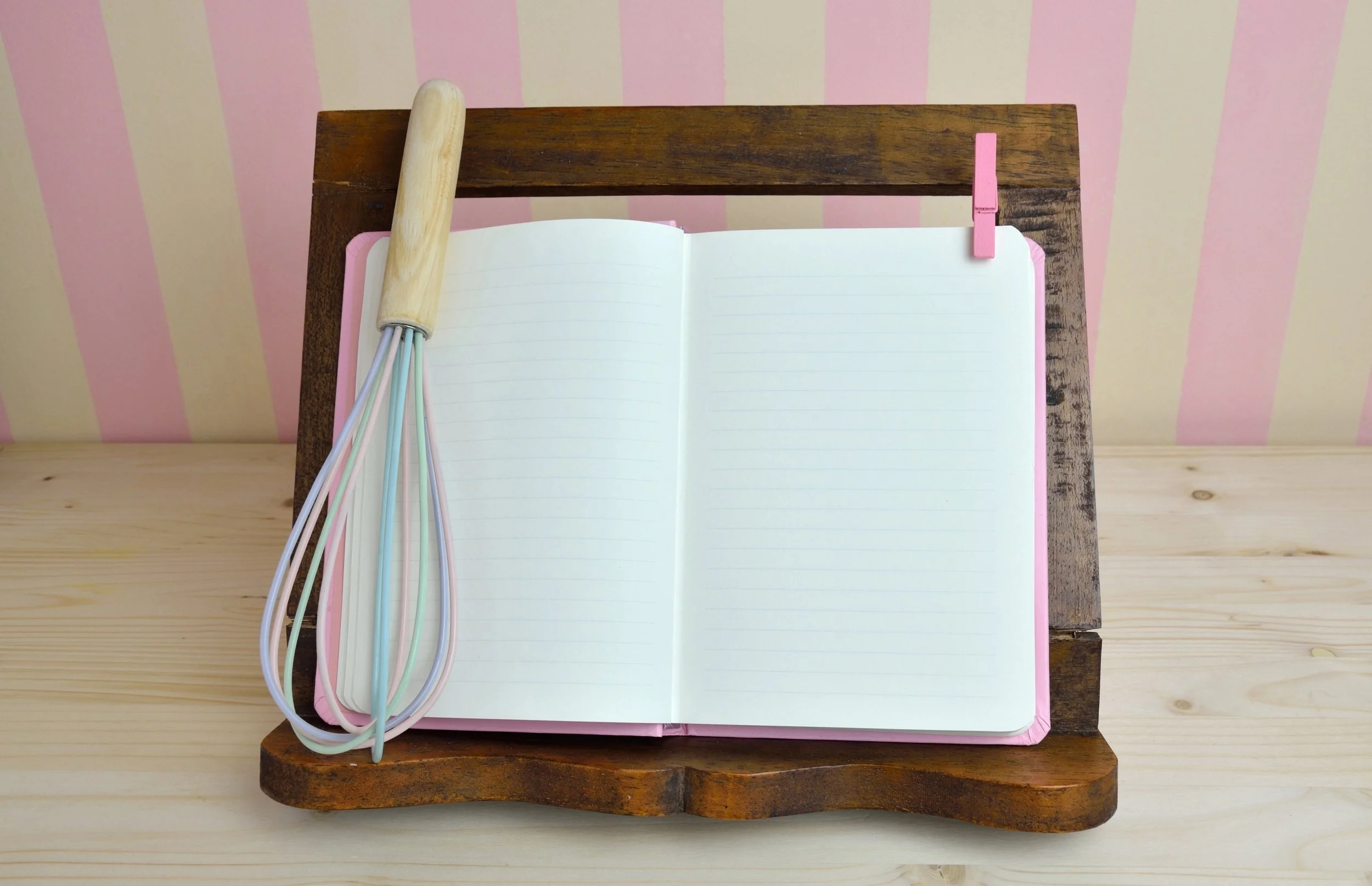 A cookbook on an easel stand holding it upright, with a whisk tilted up against it