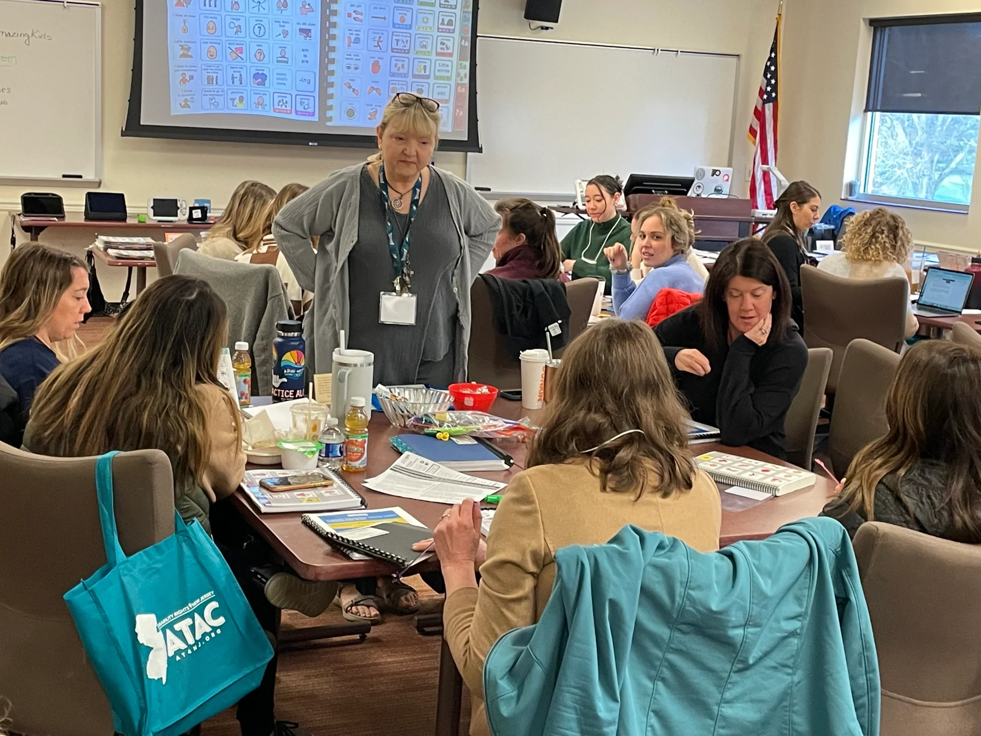 a woman standing in a classroom setting talking to people working at a table