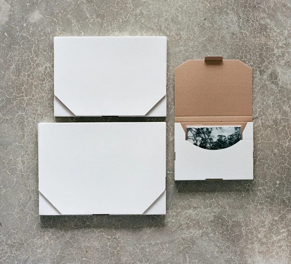 Three white closed storage boxes and one open box with a cardboard top, on a cracked concrete surface. At Atkins Photo Lab.