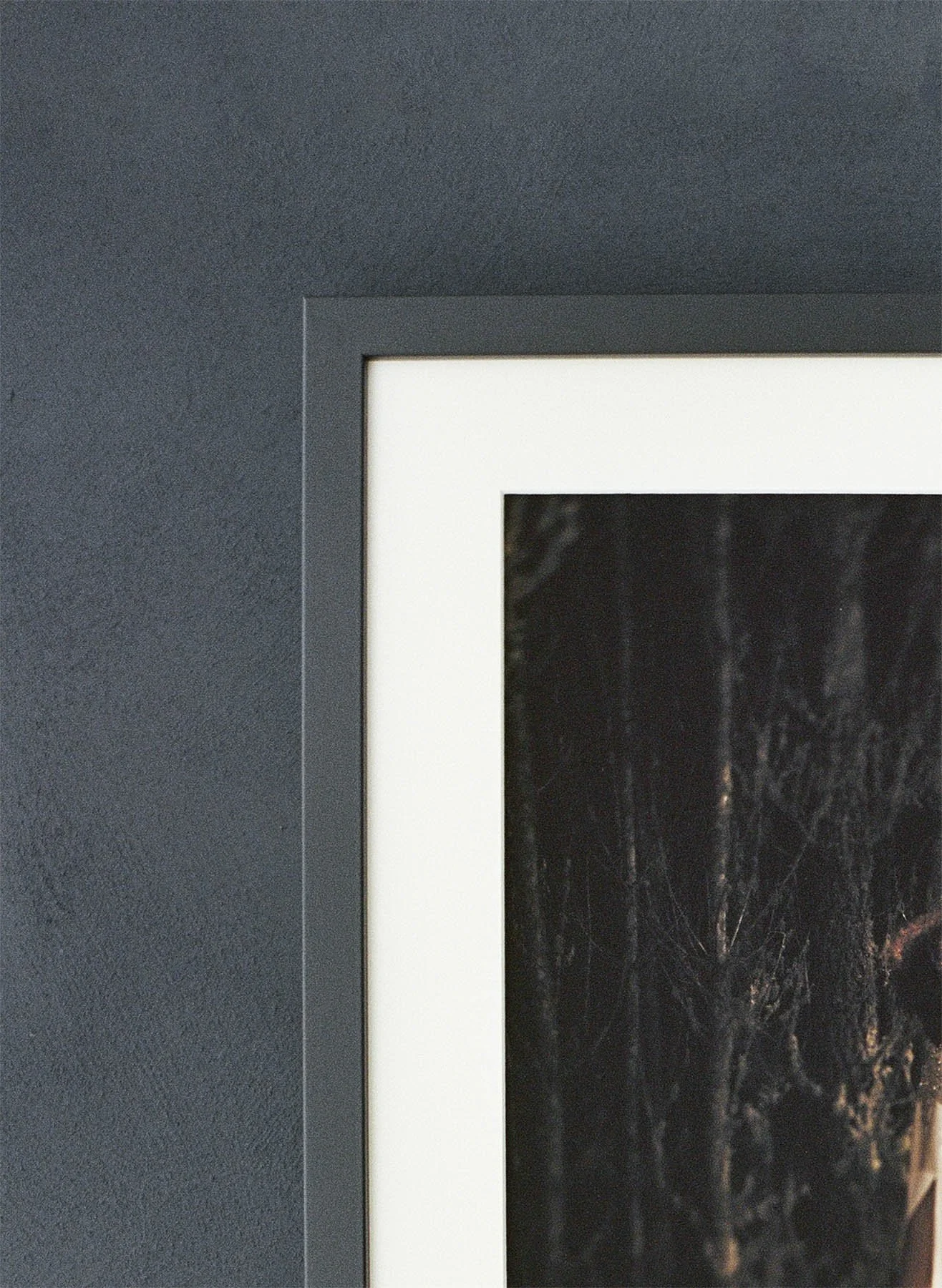 Close-up of a black picture frame with white border on a dark gray textured wall, containing a dark abstract image.