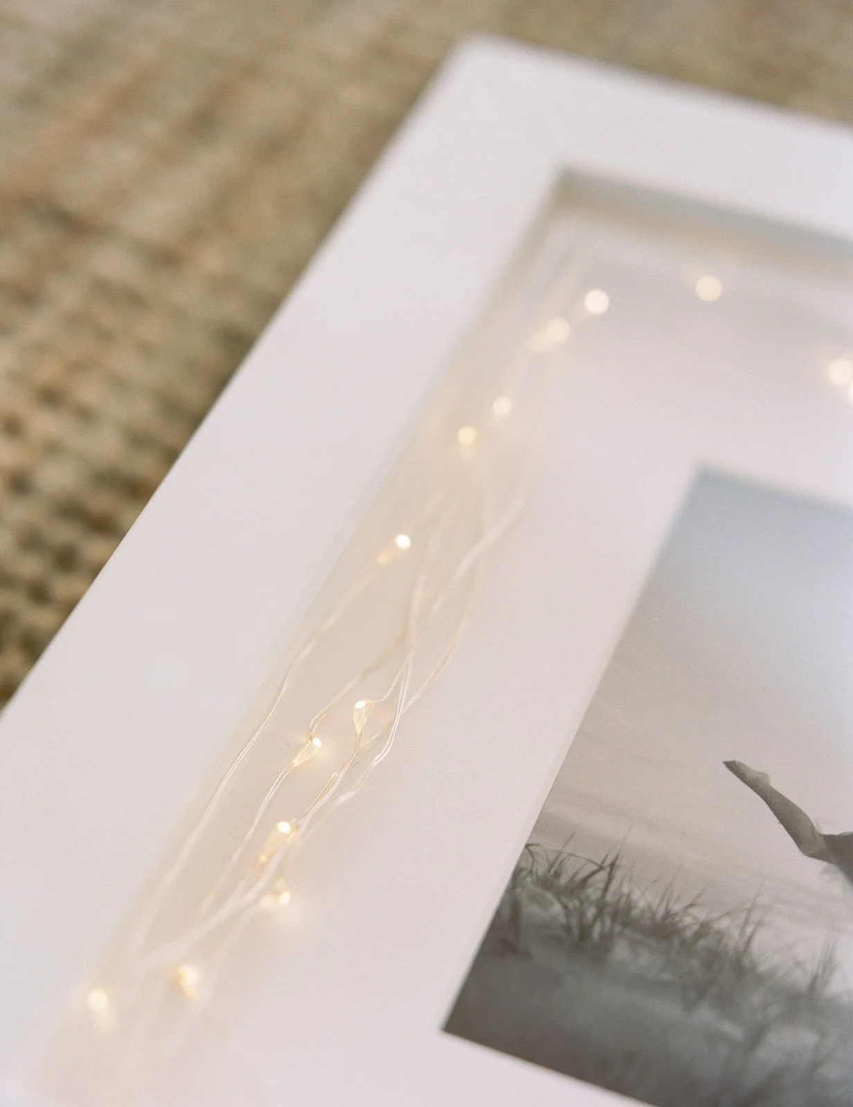 Close-up of a framed photograph with a string of white fairy lights resting on it, placed on a textured surface.
