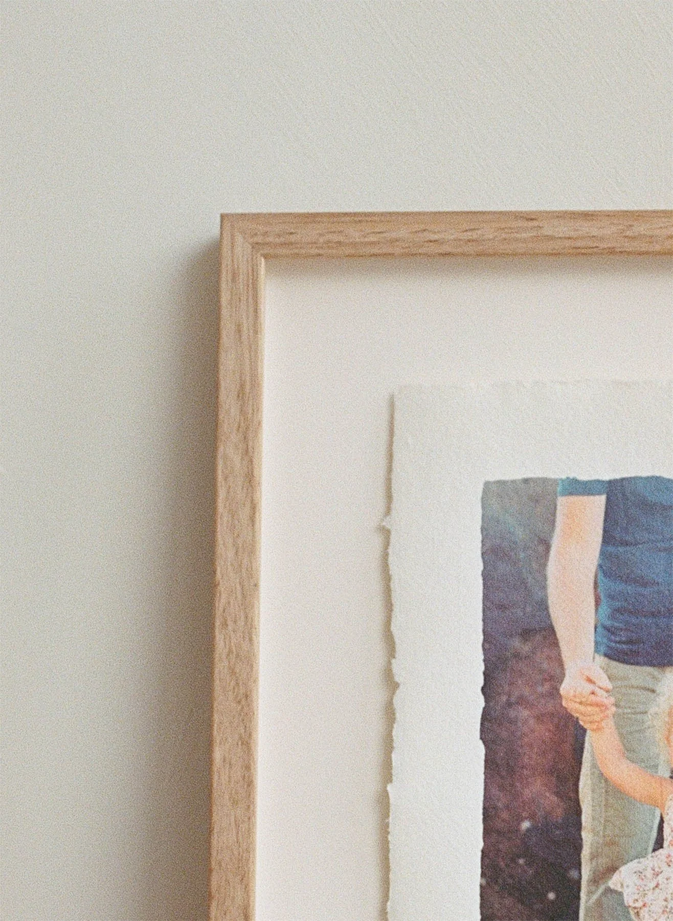 Close-up of a wooden frame around a photo, with part of the photo showing a person holding a child's hand.