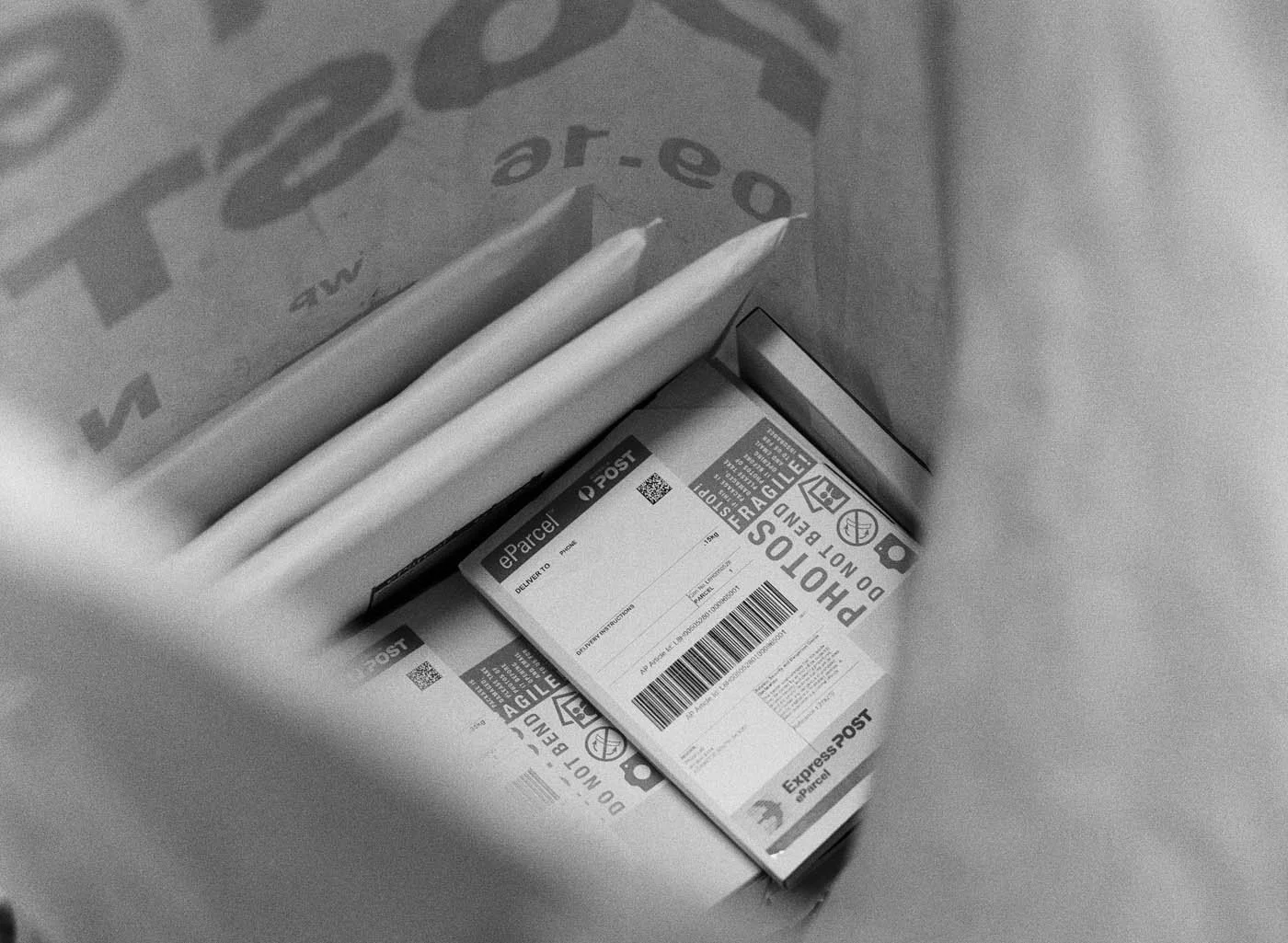 A package bag and two parcels inside a box, with shipping labels and barcodes visible. One parcel has a label with the text 'DO NOT BEND' and a warning icon at Atkins Photo Lab.