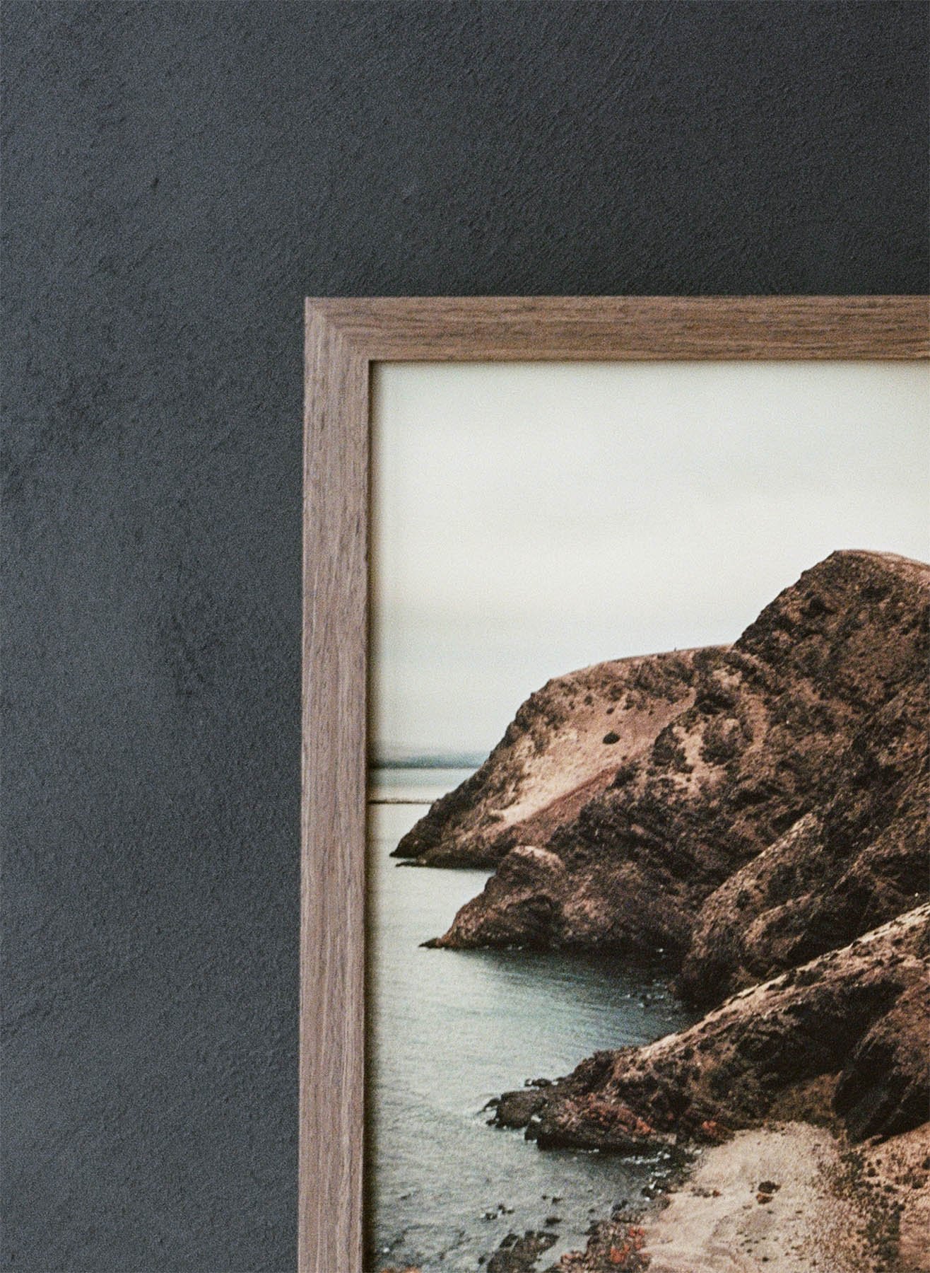 Close-up of a framed landscape photograph showing rocky coastline and water, against a dark textured wall.