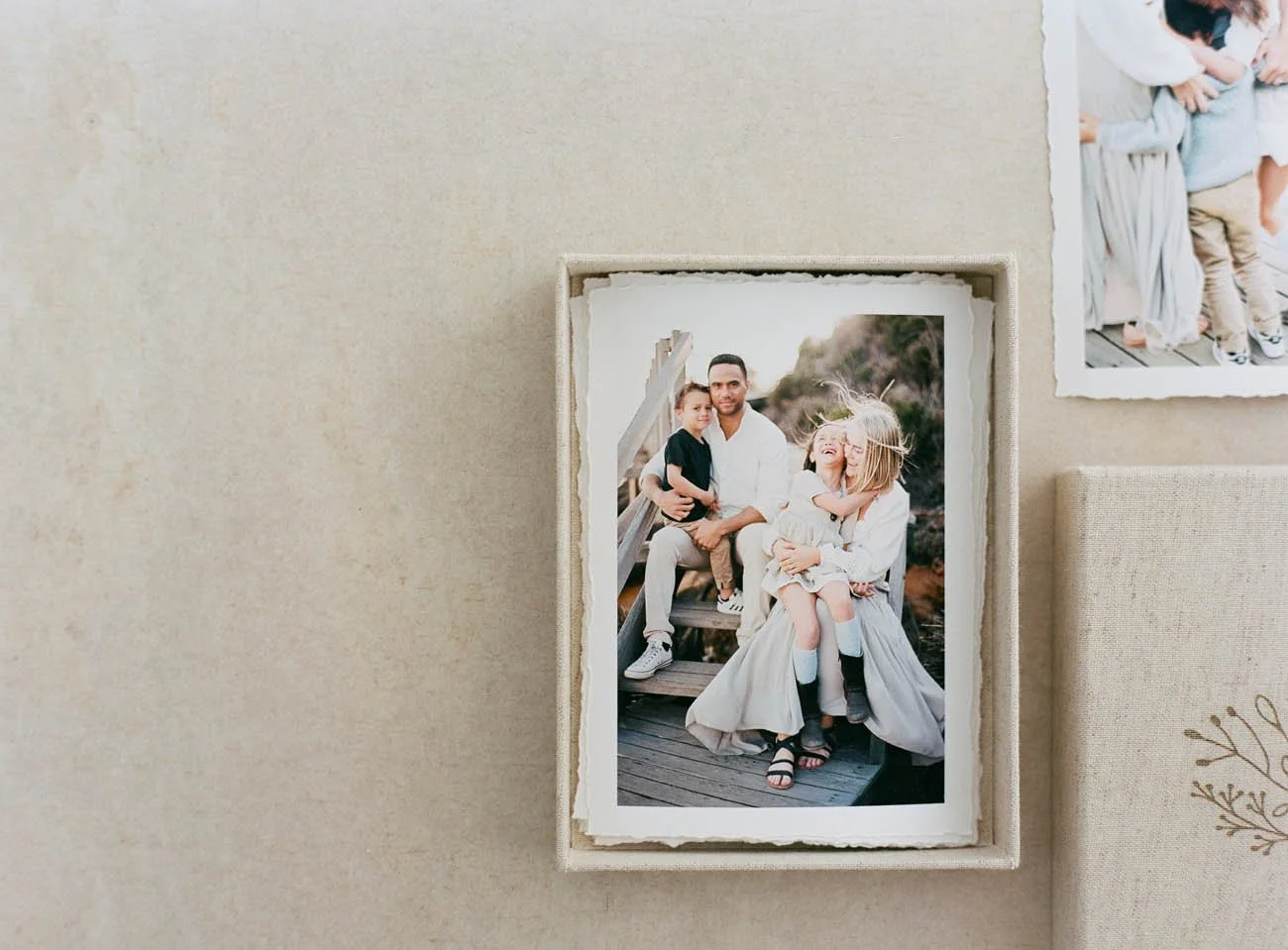 Family photo of a man, woman, and two children sitting outdoors on a wooden staircase with mountain landscape in the background.