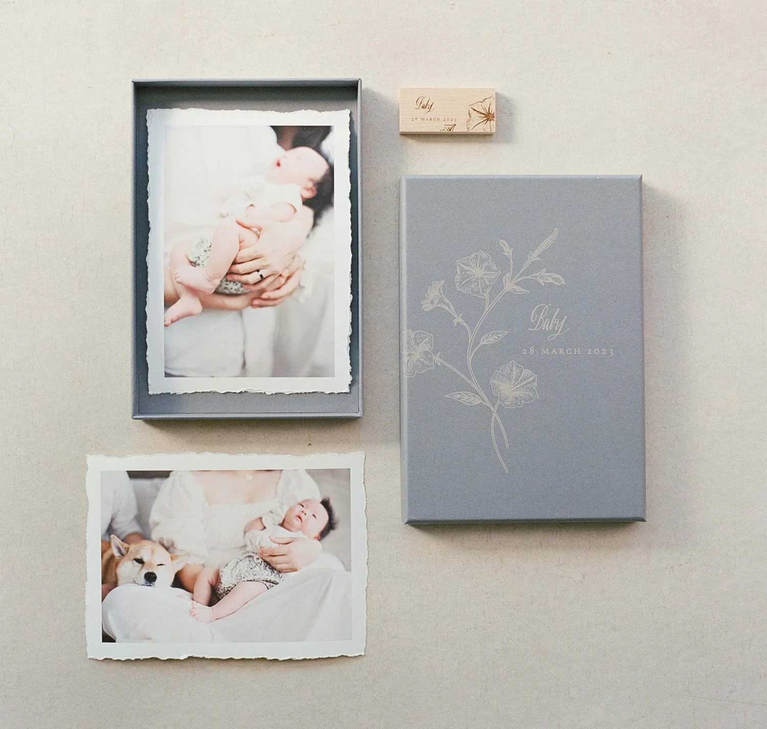 A display with a framed photo of a person holding a baby, another photo of a baby with a dog, a grey box labeled 'Baby' with a floral design and the date March 28, 2023, and a small card with handwritten text and a leaf design.