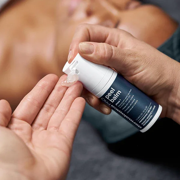 A person applying clear aloe vera gel or balm from a pump bottle onto another person's fingers, with a blurred background of a person lying down.