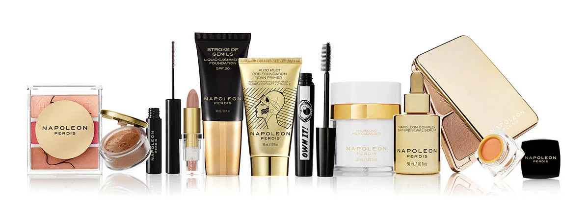 Collection of Napoleon Perdis makeup products including blush, foundation, primer, mascara, eyeliner, skincare, and lipstick in gold and black packaging.