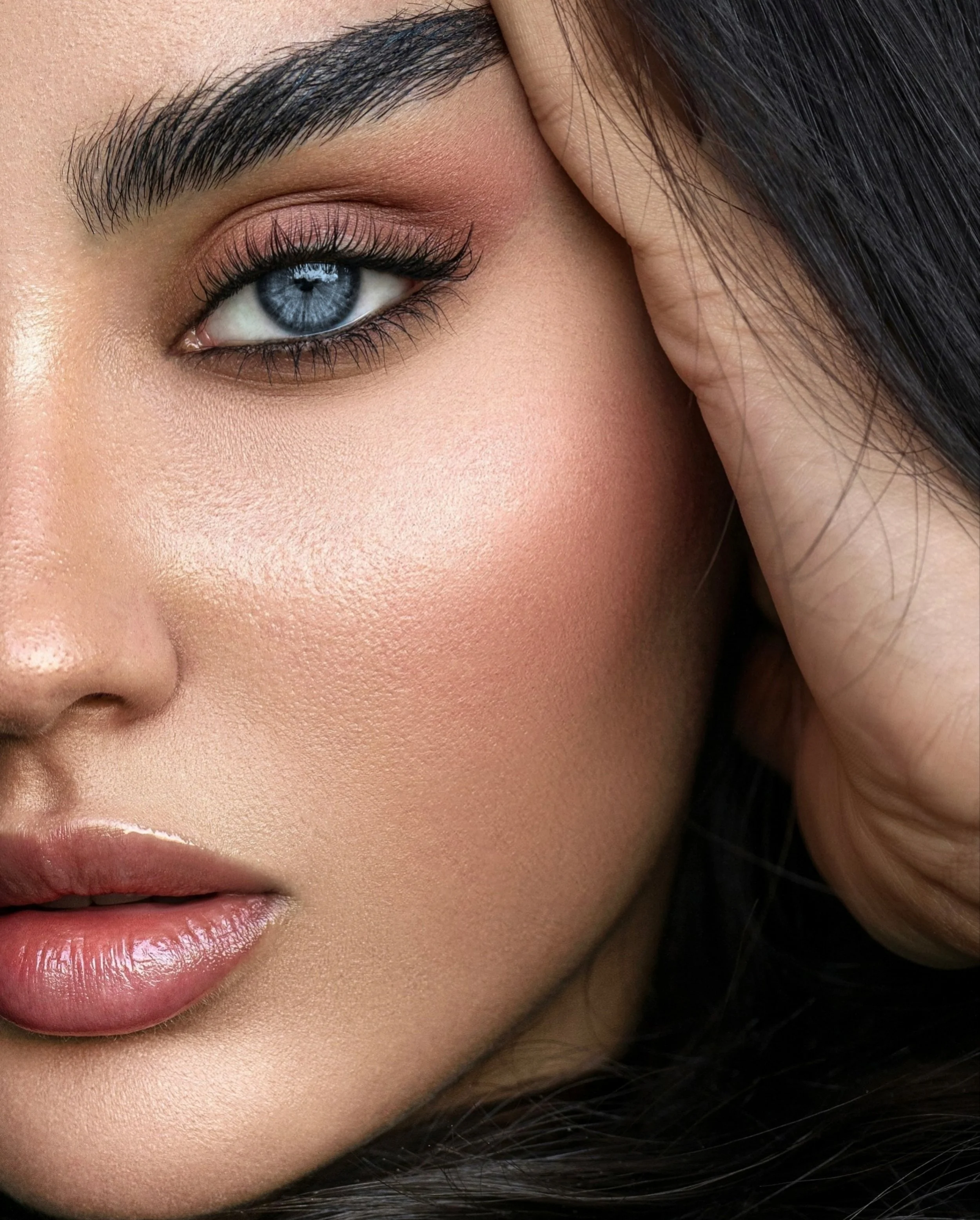 Close-up of a woman's face: blue eye, well-groomed eyebrows, pink eye makeup, full lips, and dark hair.