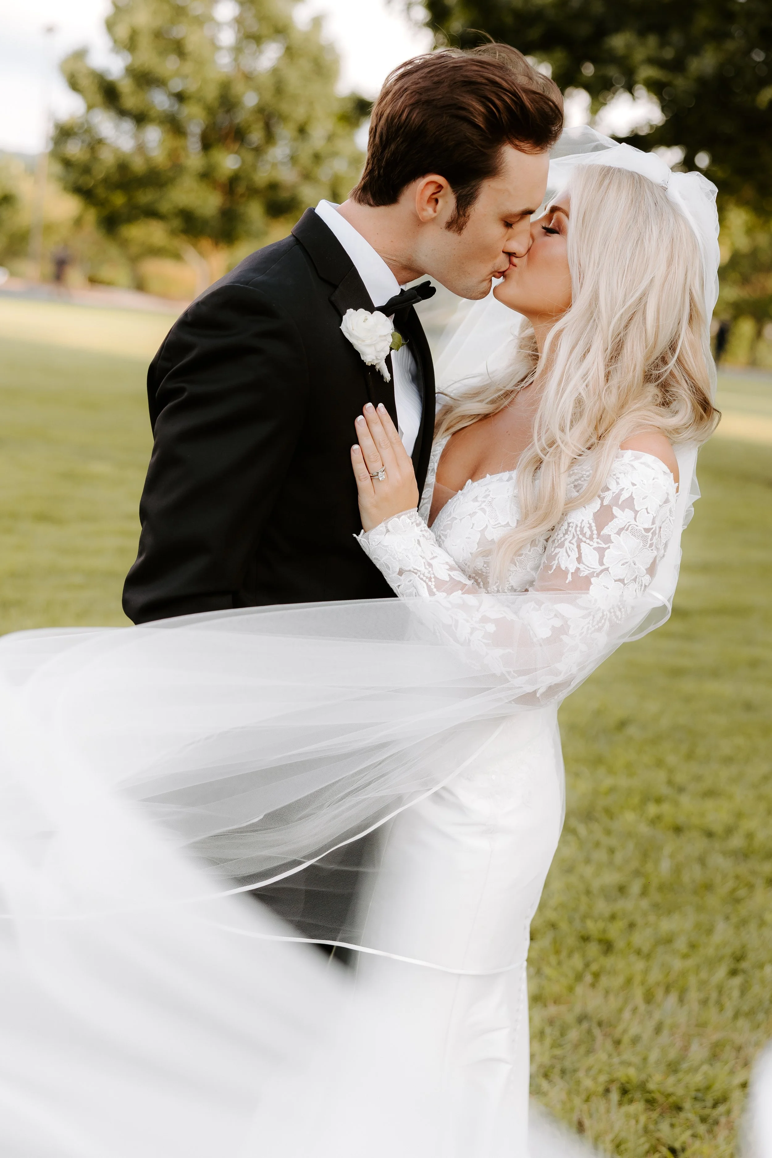 Bride and groom share a romantic kiss as the veil flows in the wind during their outdoor Nashville wedding. It is a bright and colorful true to life style photo