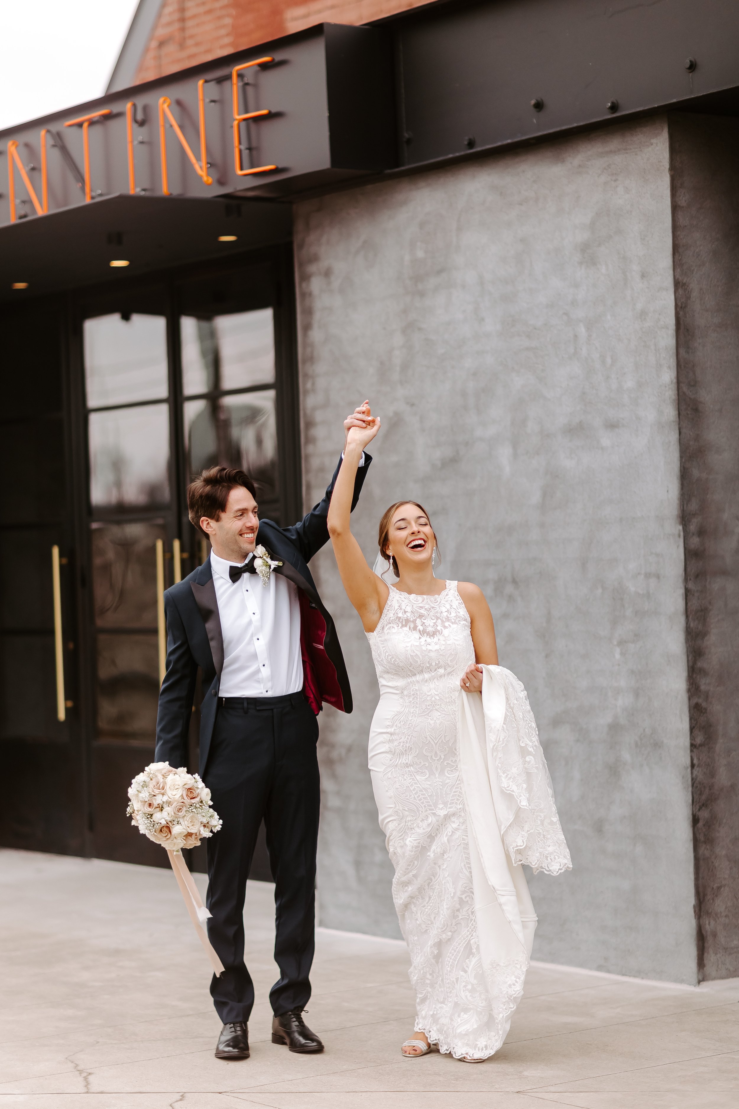 Just married couple celebrating in front of The Clementine venue in downtown Nashville, bride holding her bouquet high with laughter.