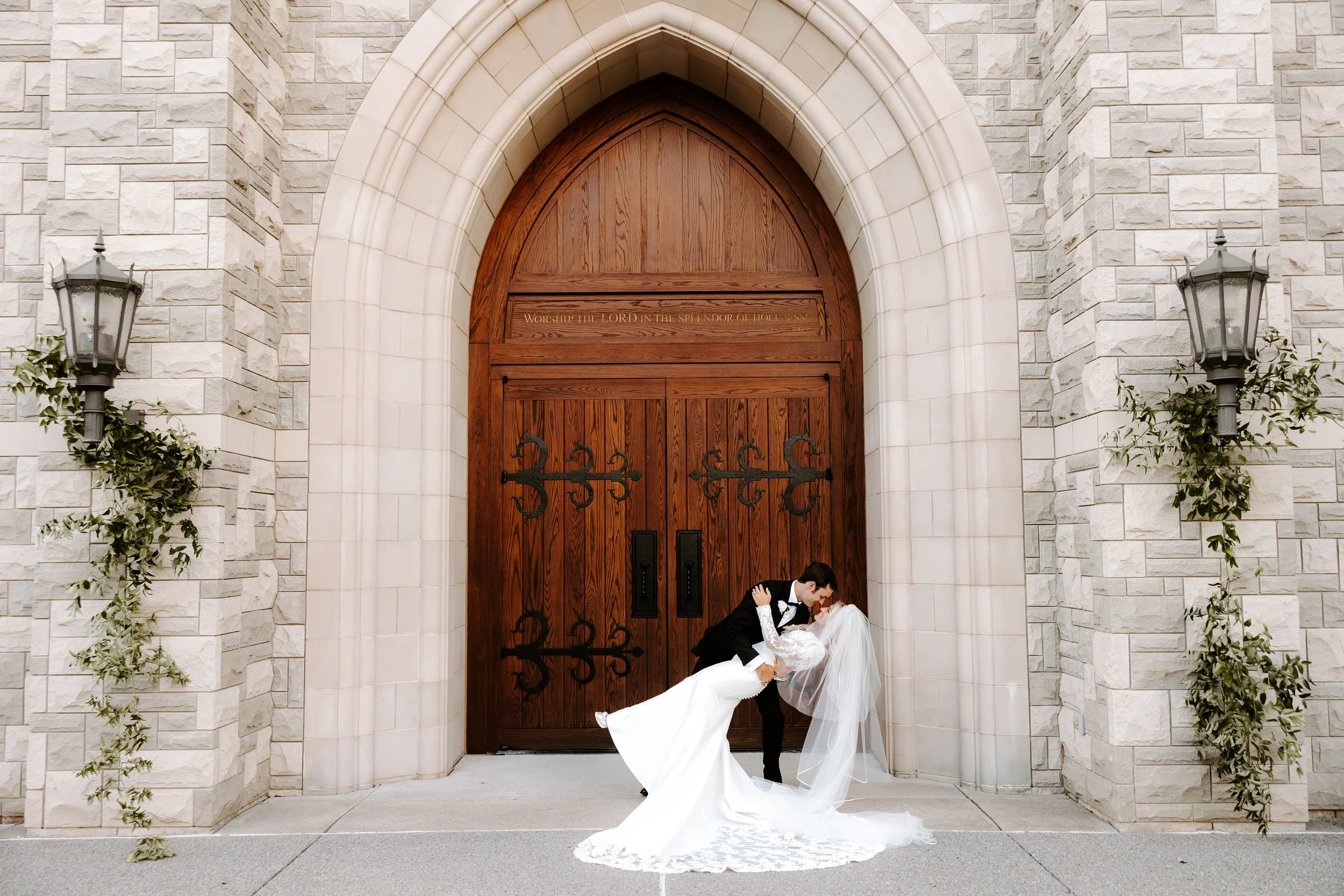 Modern romantic wedding portrait outside a stone chapel in Austin, bride and groom  sharing a kiss while dipping in front of arched wooden doors.