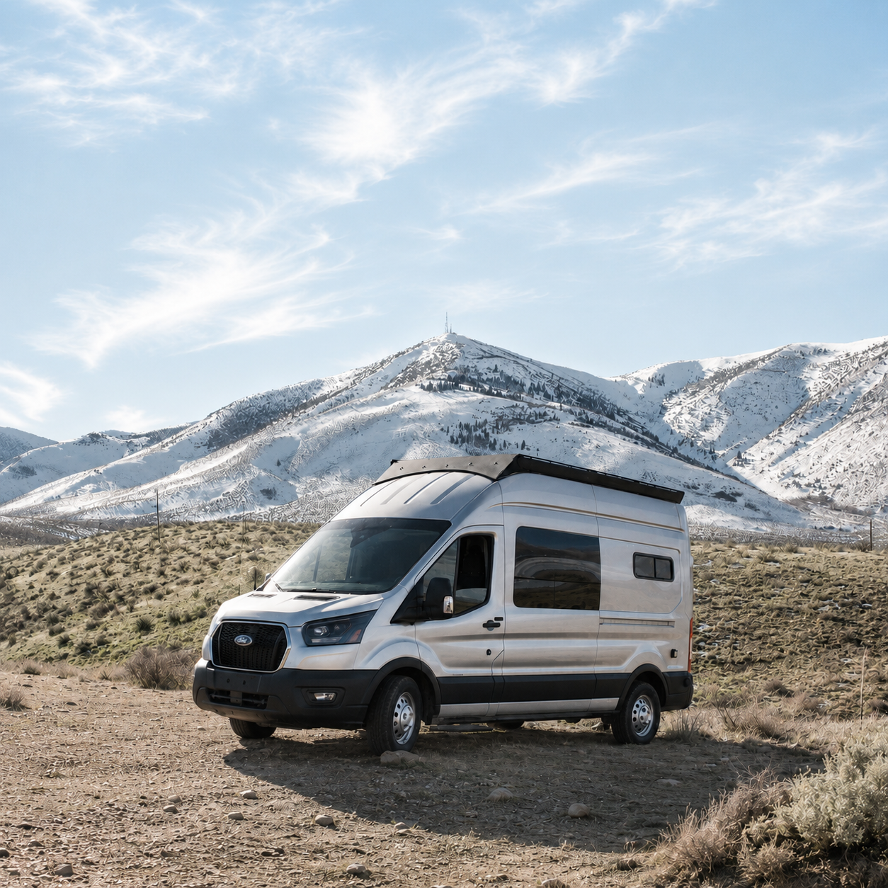Ford Transit 148 astronomy camper van parked on a dirt road below snowy mountains and blue sky