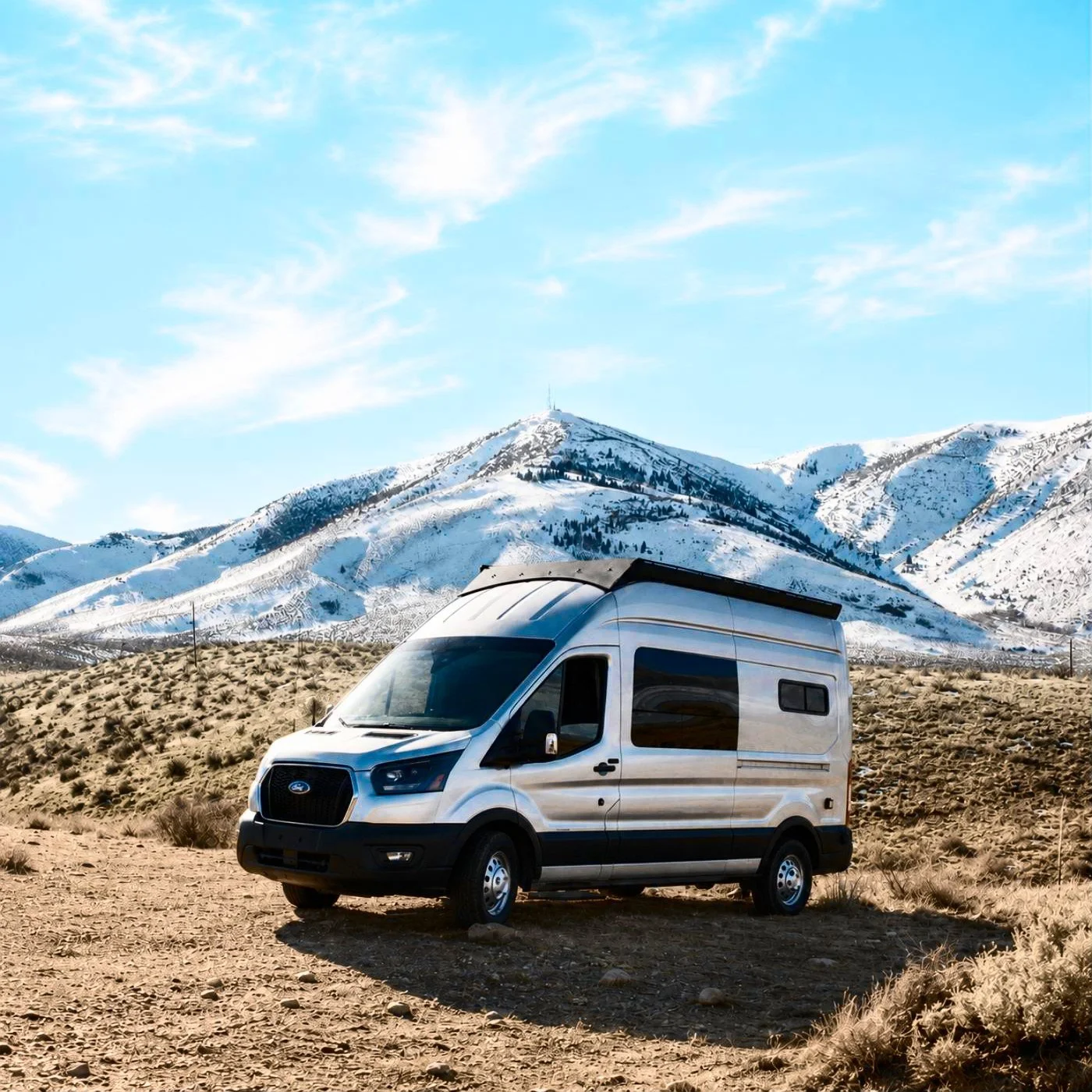 Ford Transit 148 astronomy camper van parked on a dirt road below snowy mountains and blue sky