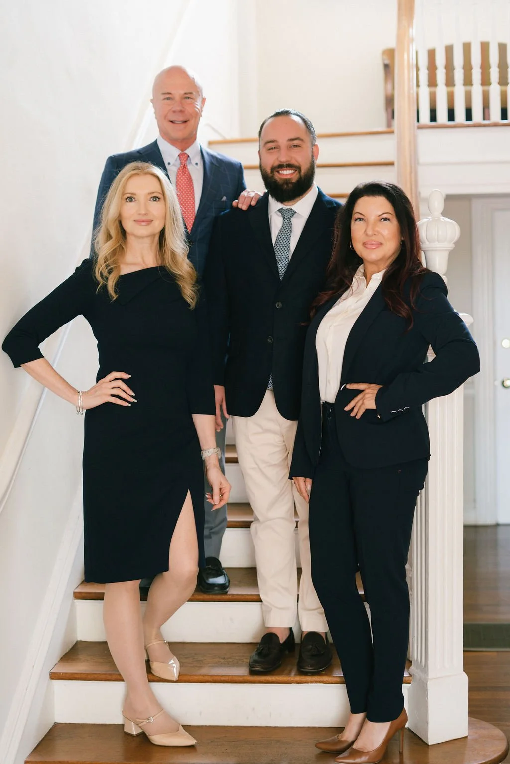 Four professionally dressed adults standing on a staircase indoors, smiling at the camera.
