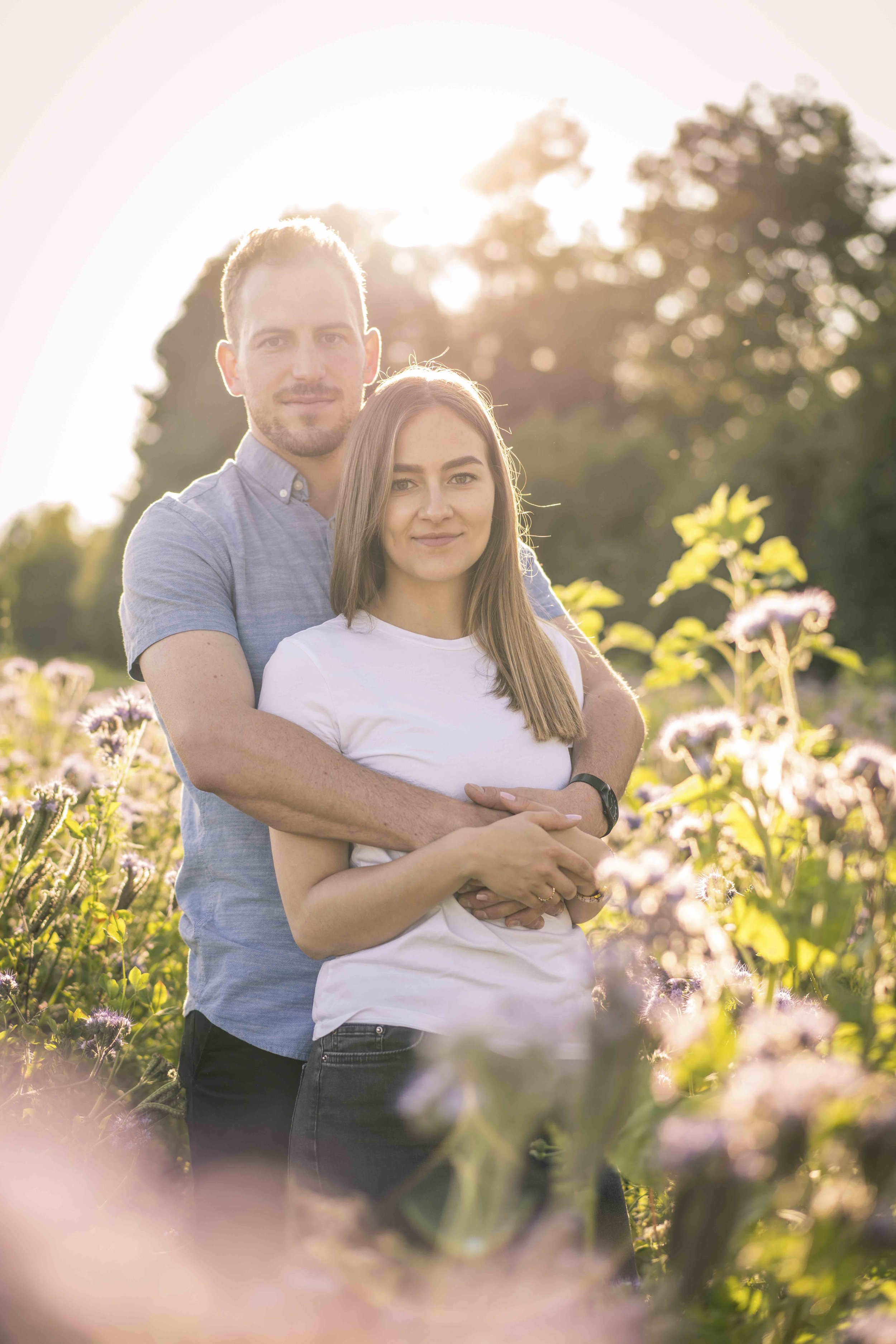 Ein Paar, das sich im Freien umarmt, umgeben von Blumen, mit Sonnenlicht im Hintergrund.