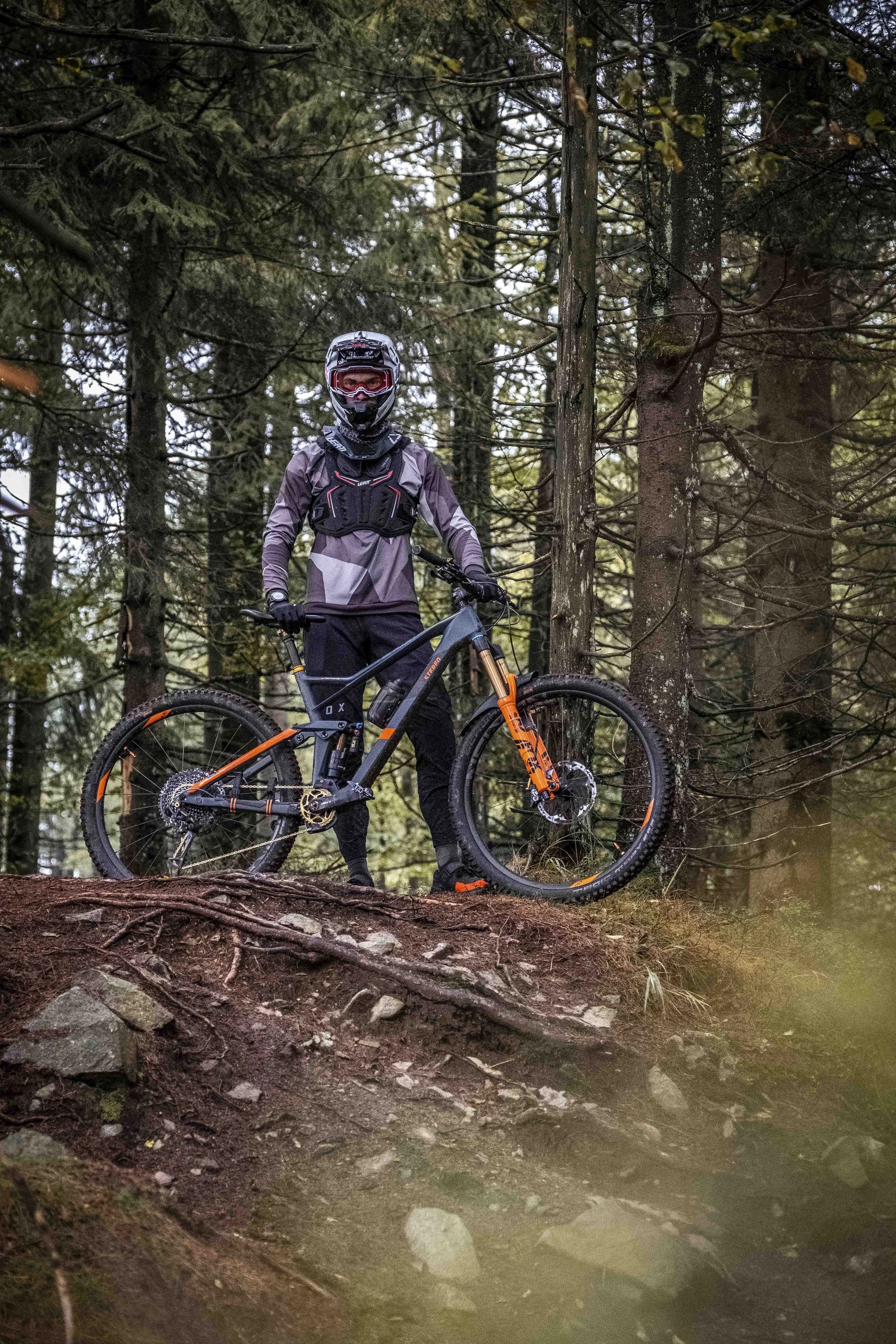 Person mit Schutzkleidung und Helm steht mit einem Mountainbike im Wald.