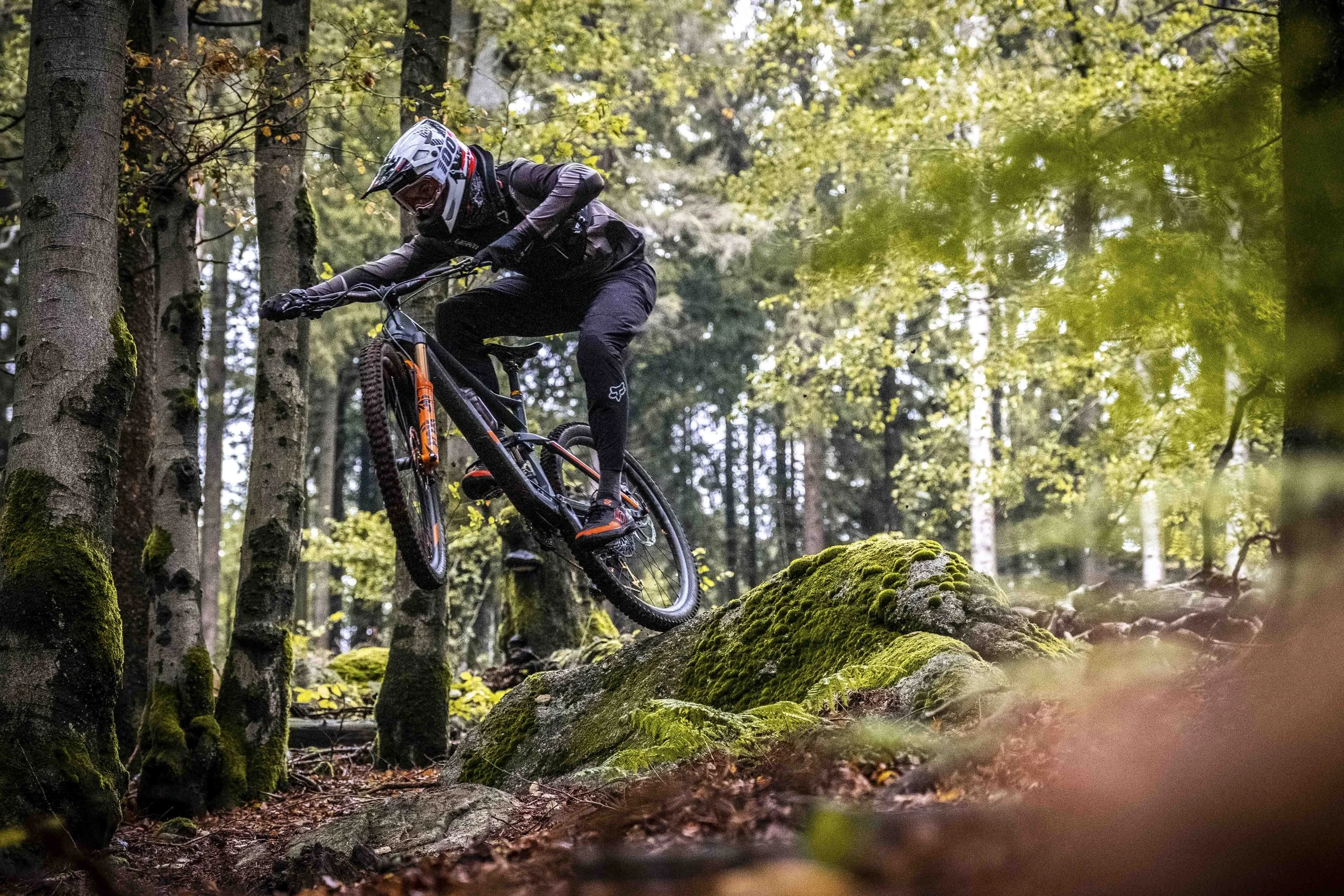 Mountainbiker in einem Wald springt über einen moosbedeckten Felsen.