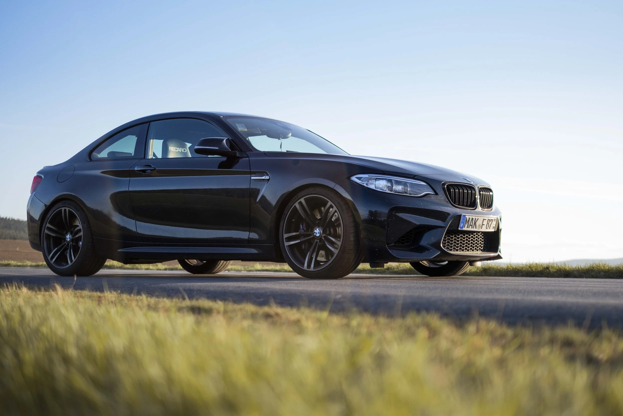 Schwarzer BMW Sportwagen auf Landstraße bei sonnigem Wetter, Seitenansicht.