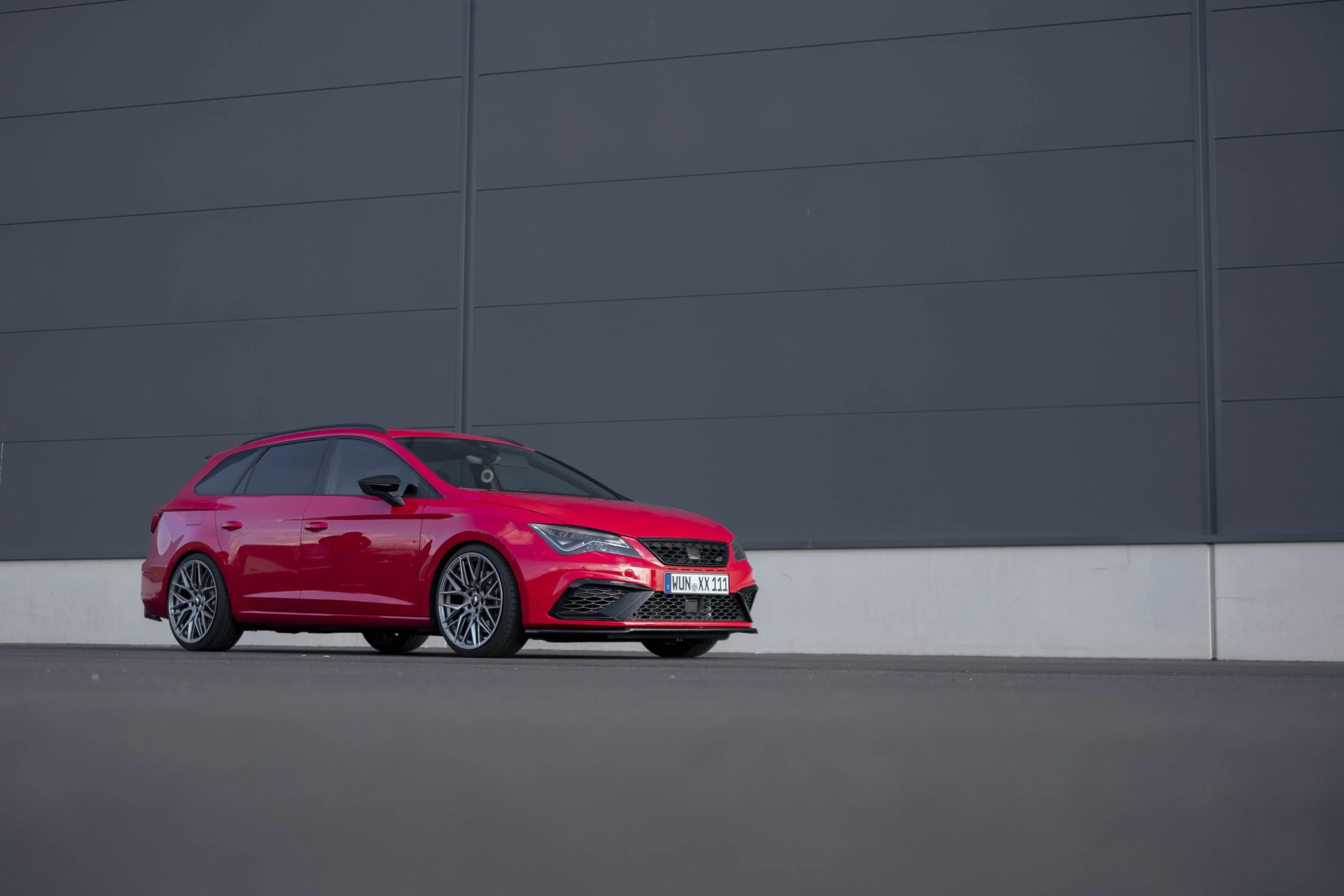 Rotes Auto, Seitenansicht, auf grauem Hintergrund in Stadtumgebung geparkt. Moderne Karosserie.