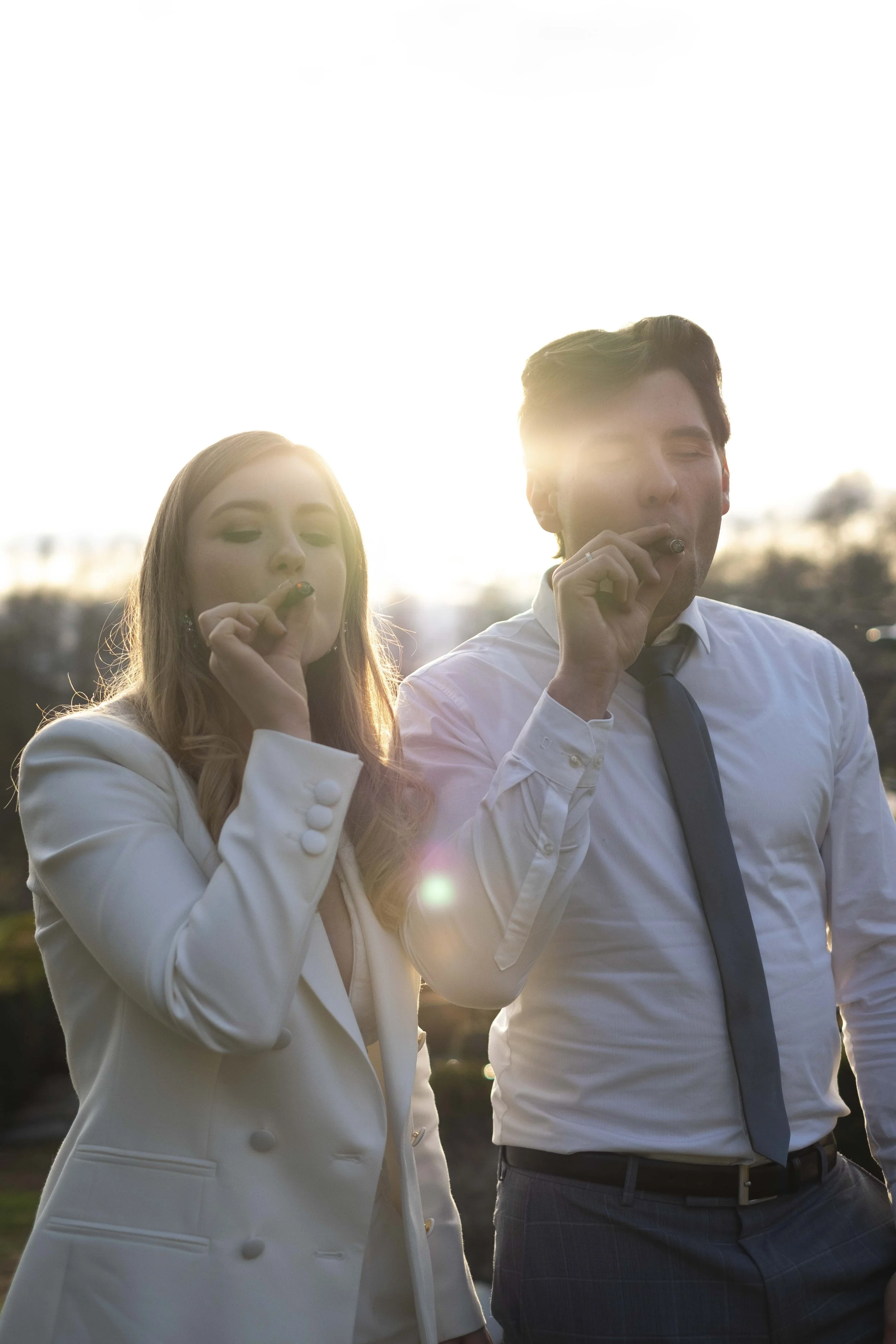 Ein Mann und eine Frau rauchen Zigarren im Freien bei Sonnenuntergang, elegant gekleidet.